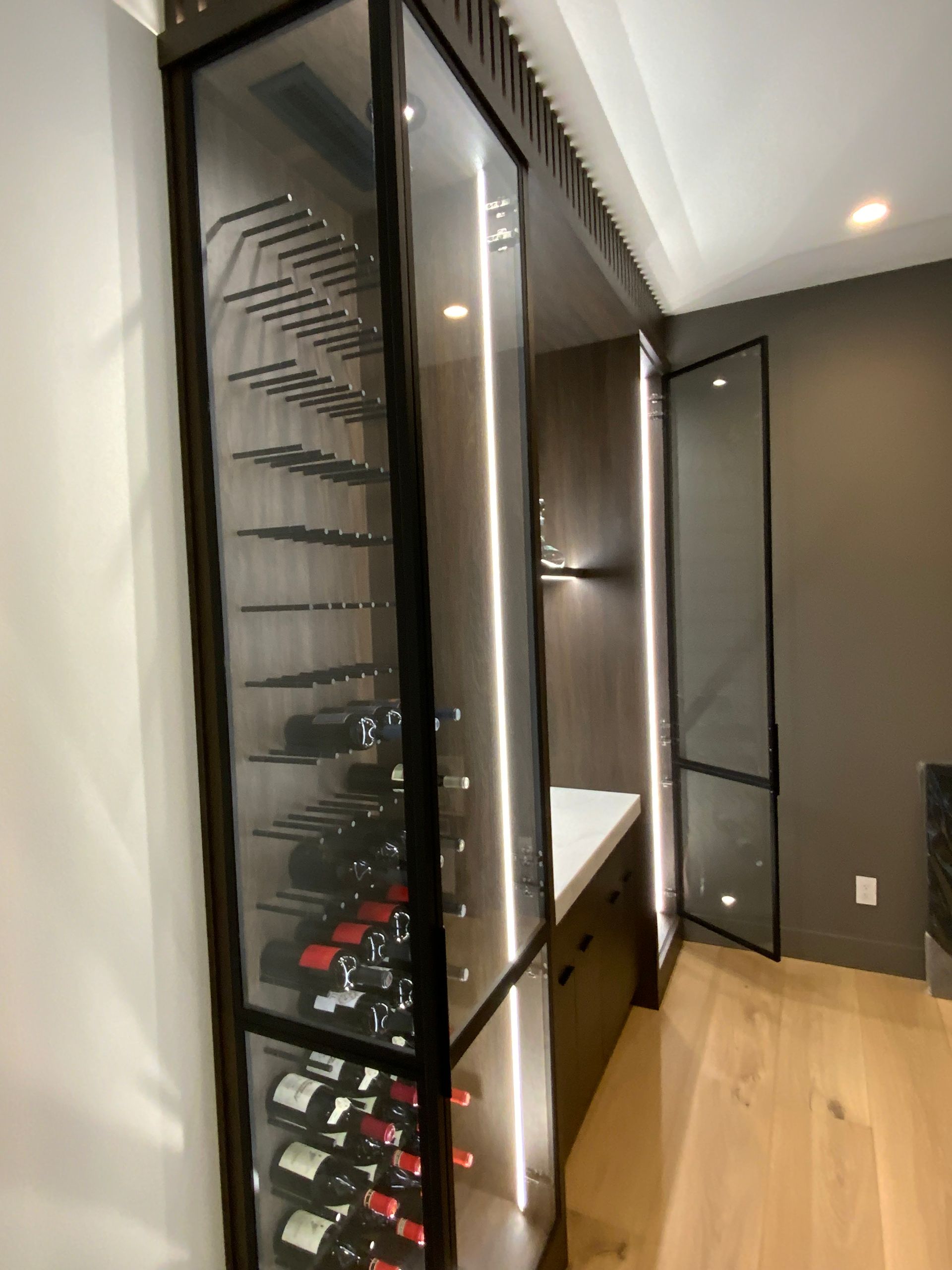 Modern wine cabinet with glass doors, interior lights, and a countertop, against a wood-paneled wall.