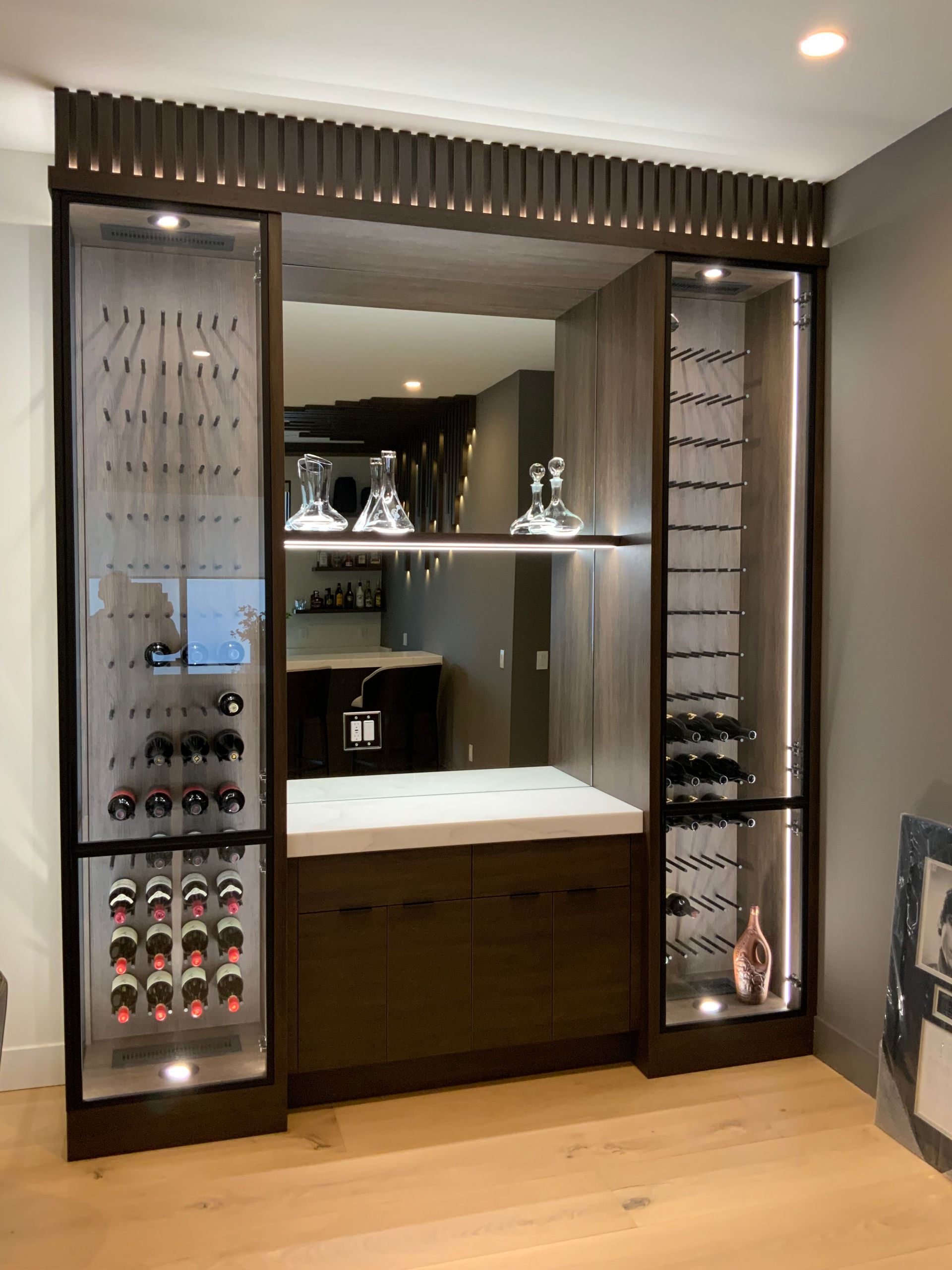 Wine storage and bar area with wood cabinets, glass shelves, and back mirror.