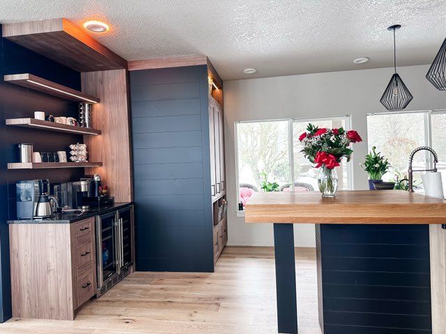 Modern kitchen with coffee station and island; dark blue and light wood tones, bright interior.