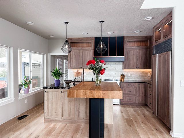 Modern kitchen with wood cabinets, island, and light wood flooring. Features include a black range hood and pendant lights.