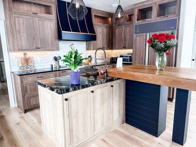 Elegant kitchen with light wood cabinets, dark blue accents, marble island countertop, and wooden island overhang.