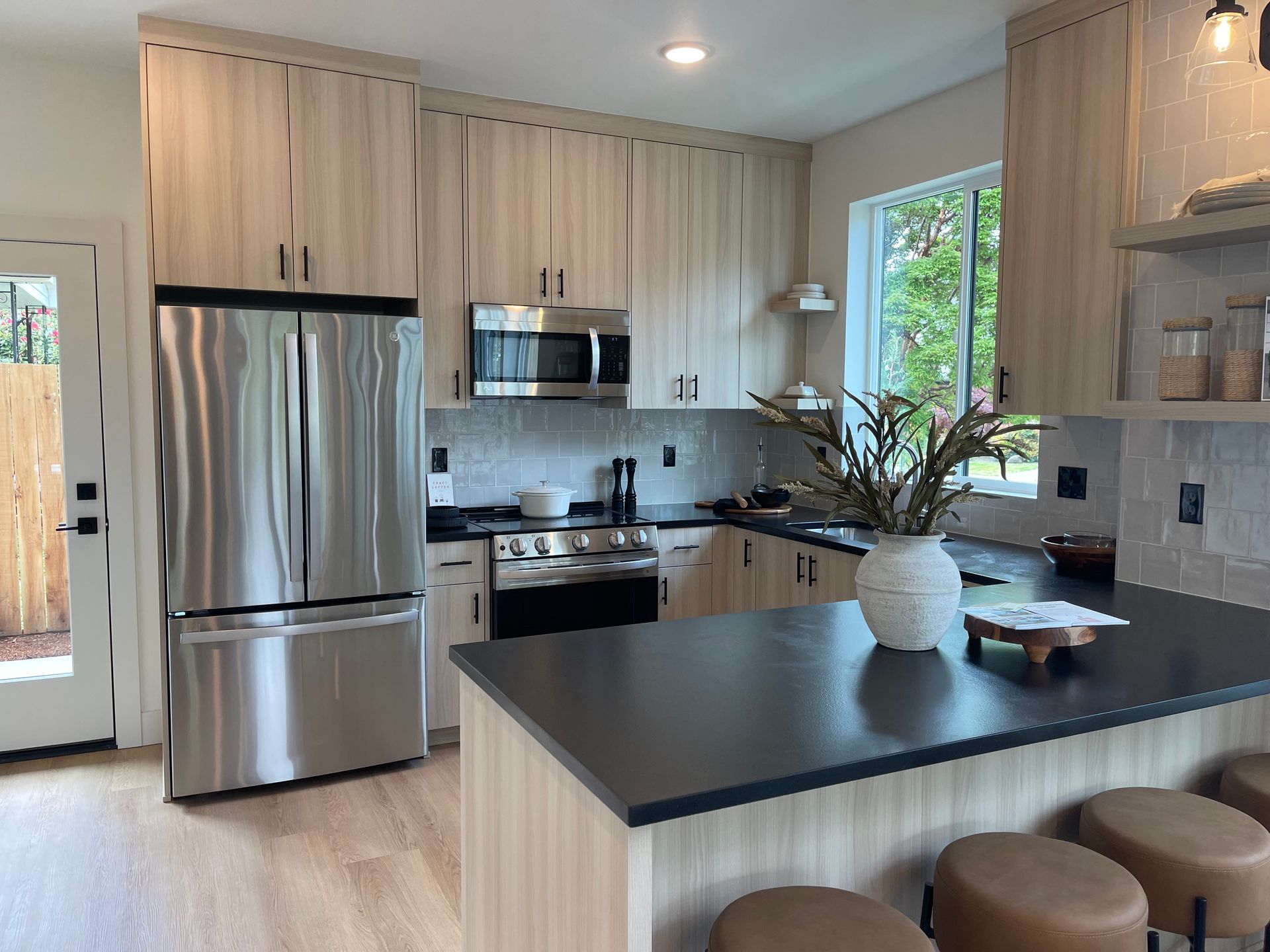 Modern kitchen with light wood cabinets, stainless steel appliances, and a dark countertop island.