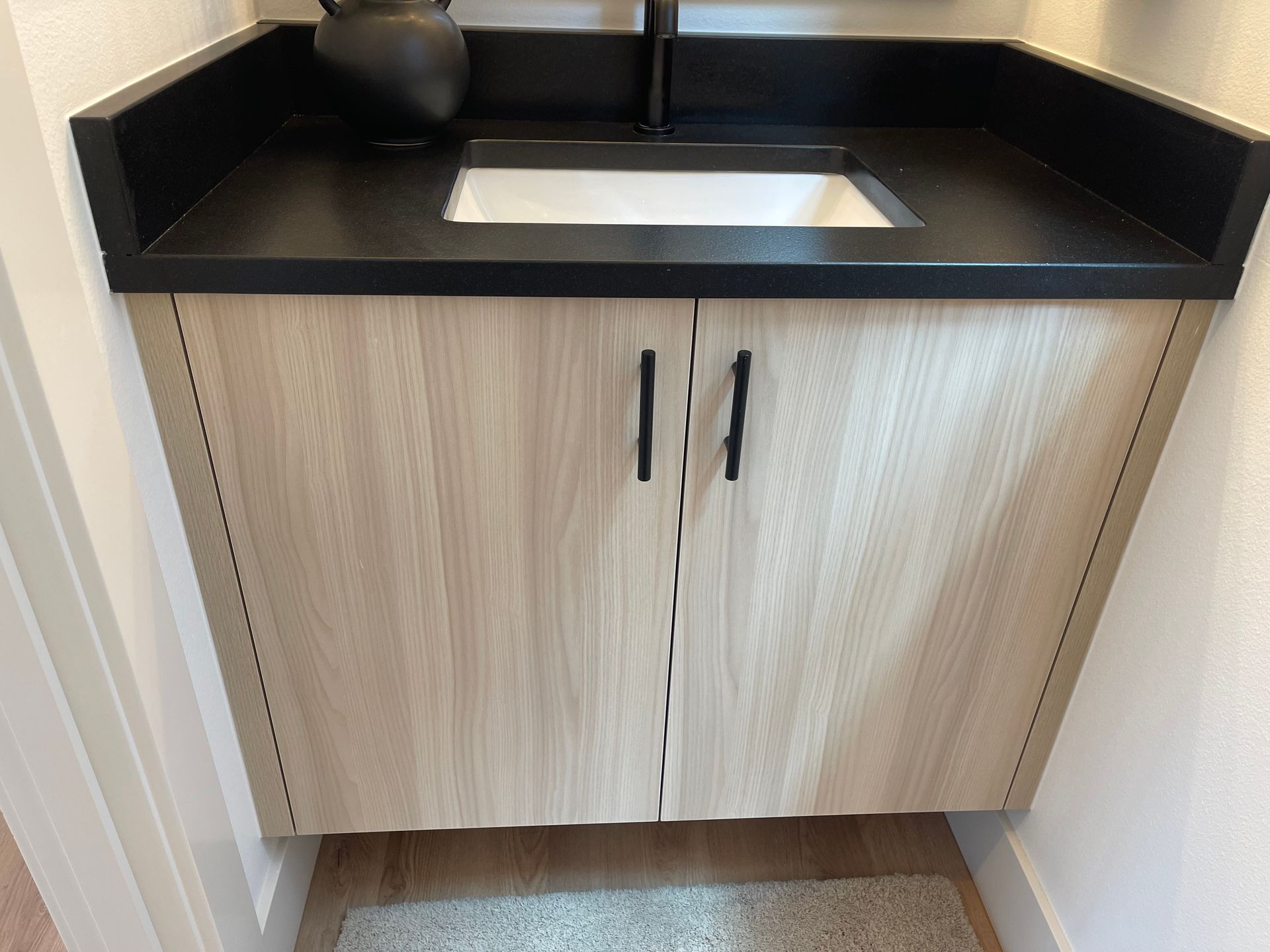Light wood bathroom vanity with black countertop, sink, and black handles.