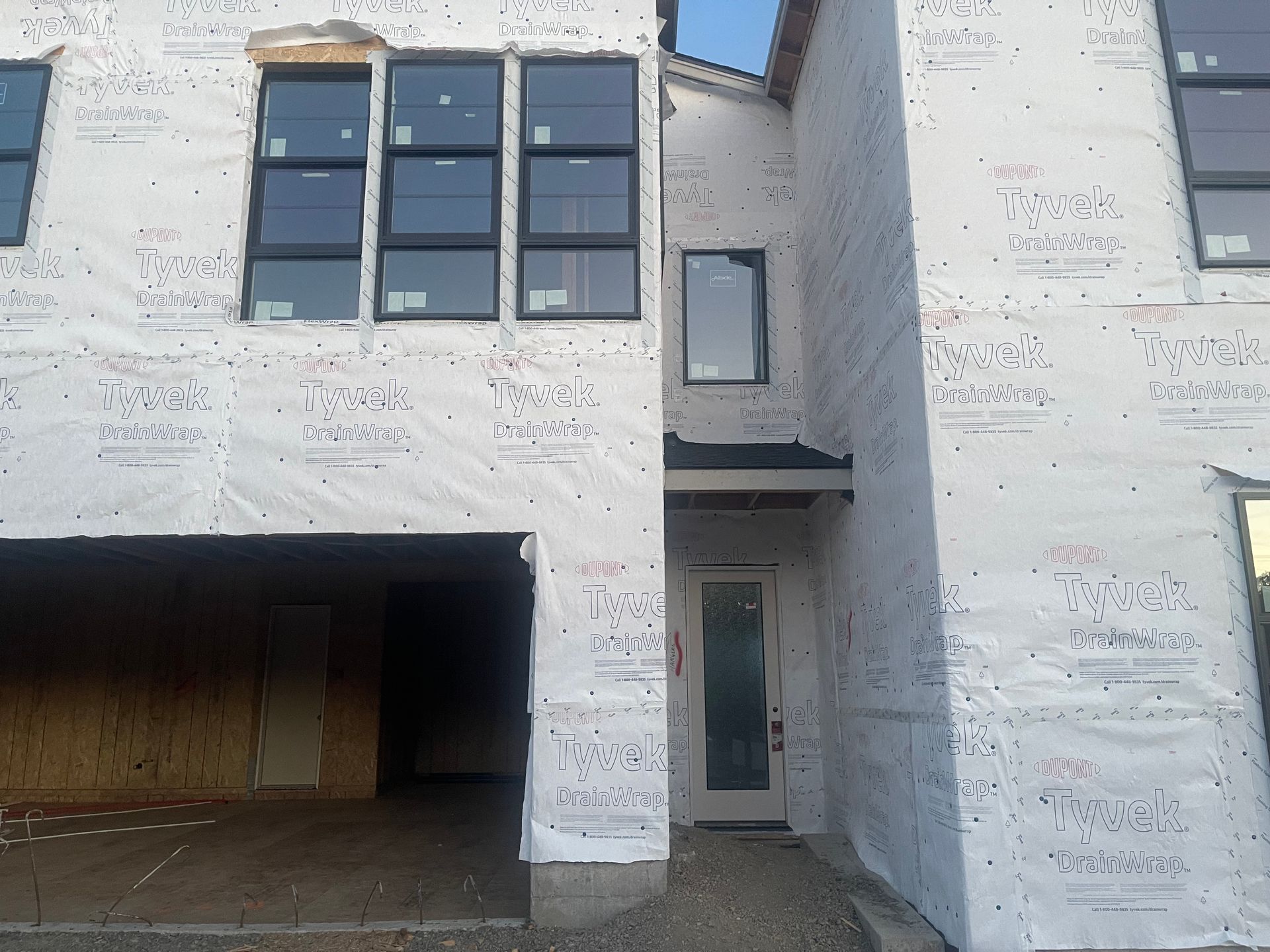 Construction of a house: garage and entrance with windows covered in white sheeting, under a blue sky.