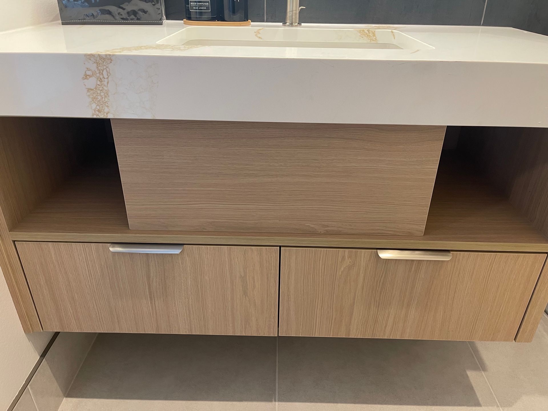 Bathroom vanity with light wood grain drawers and a white countertop with visible water stains.
