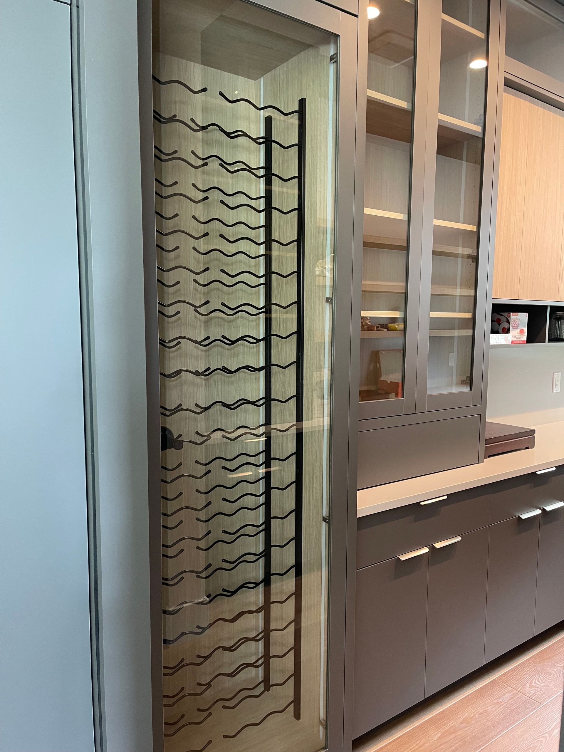 Wine rack with a glass door, built into a modern kitchen with cabinetry.