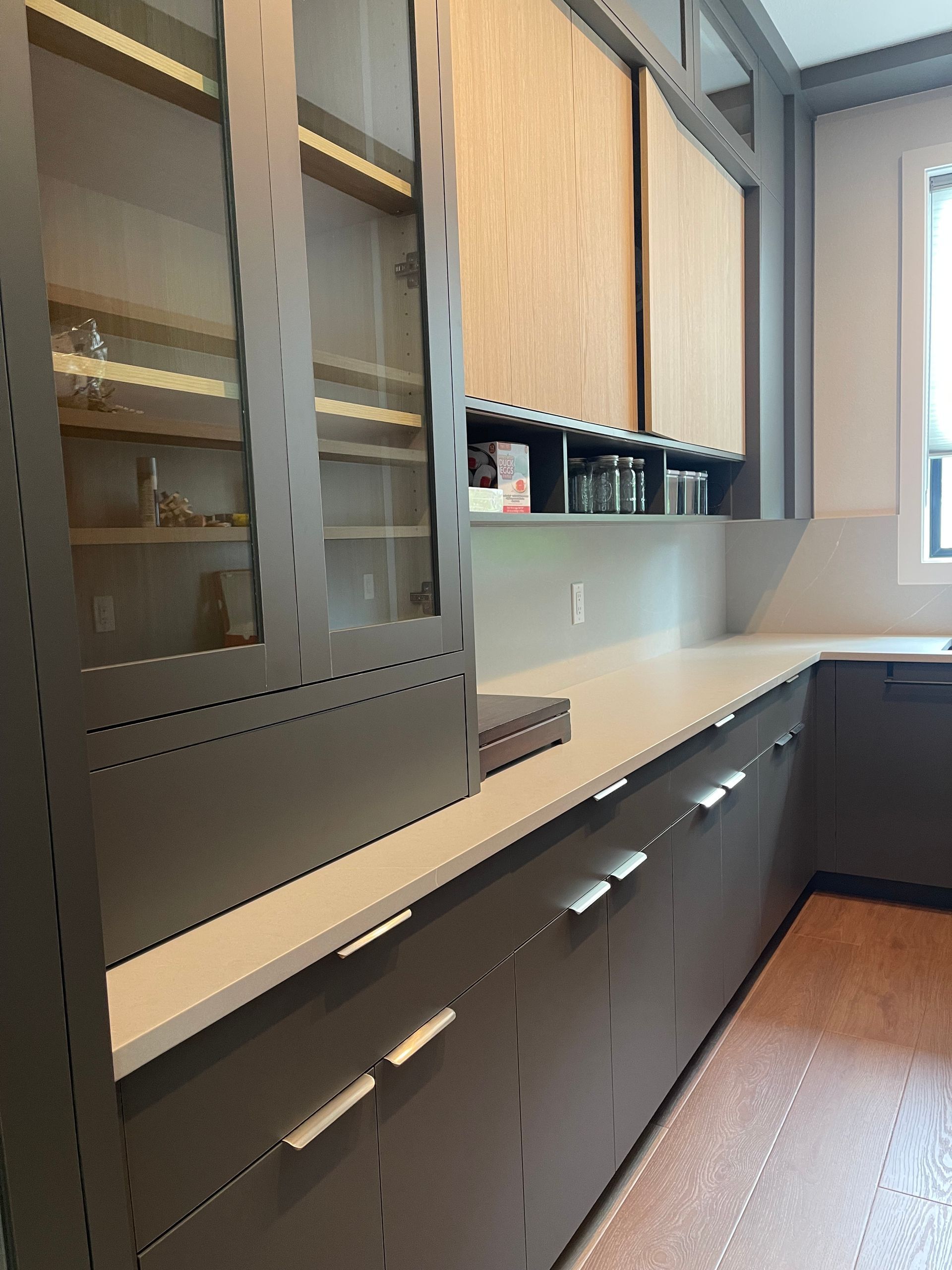 Dark gray kitchen cabinets with a light countertop and a glass-front cabinet on the left.