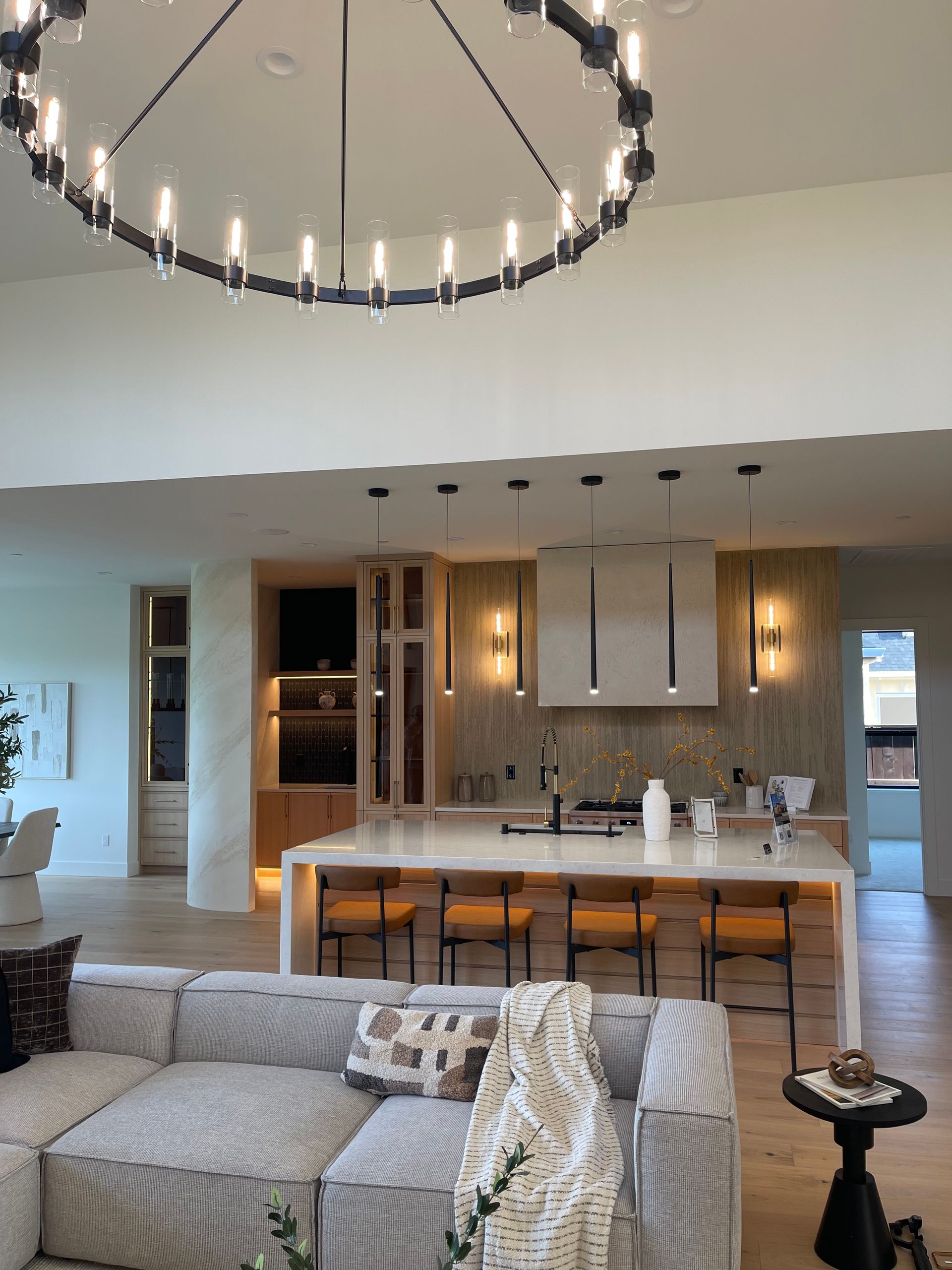 Open-plan living room and kitchen with sectional sofa, island, pendant lights, and large circular chandelier