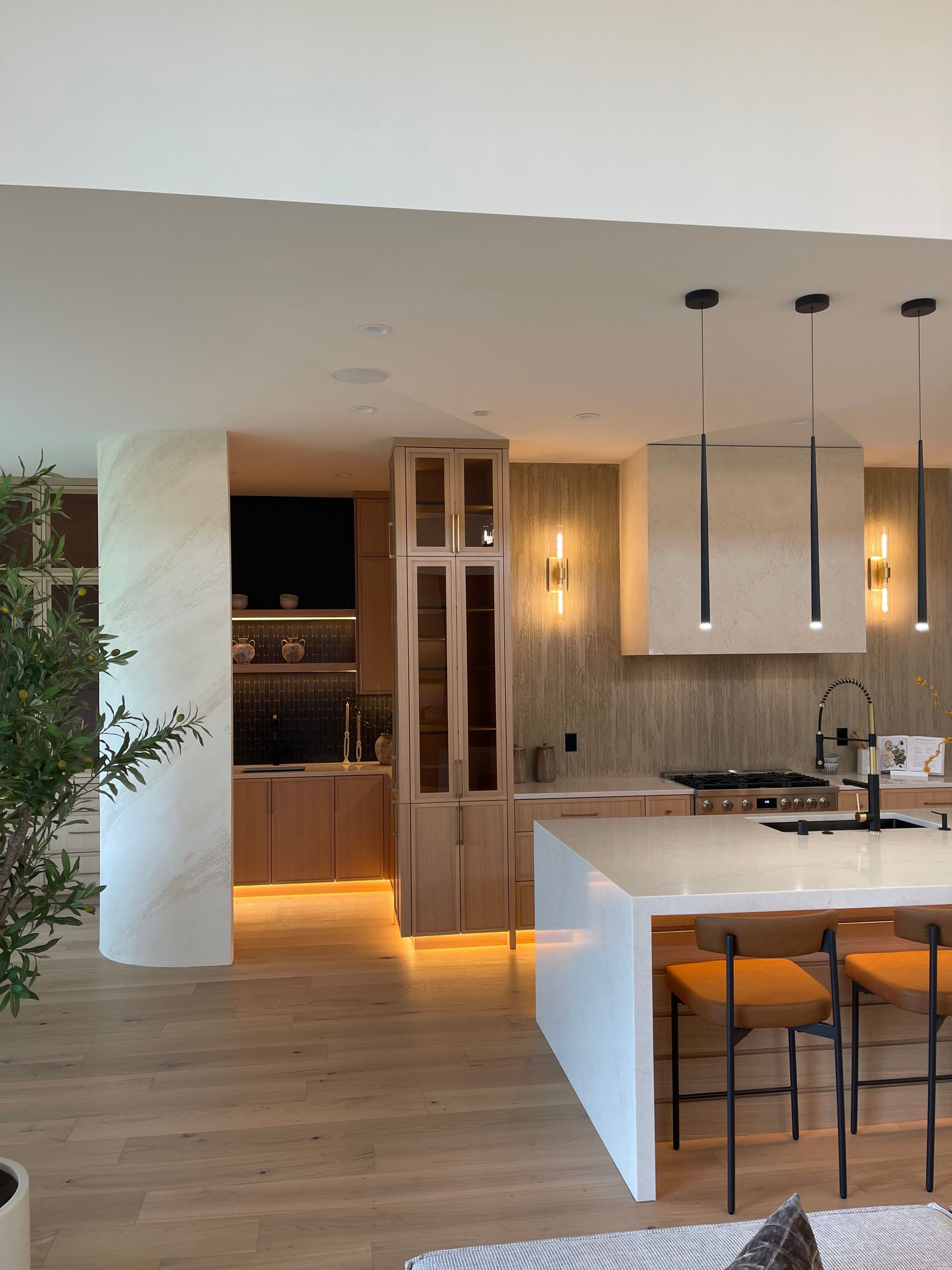 Modern open-plan kitchen with light wood floors, white cabinets, marble island, and warm under-cabinet lighting