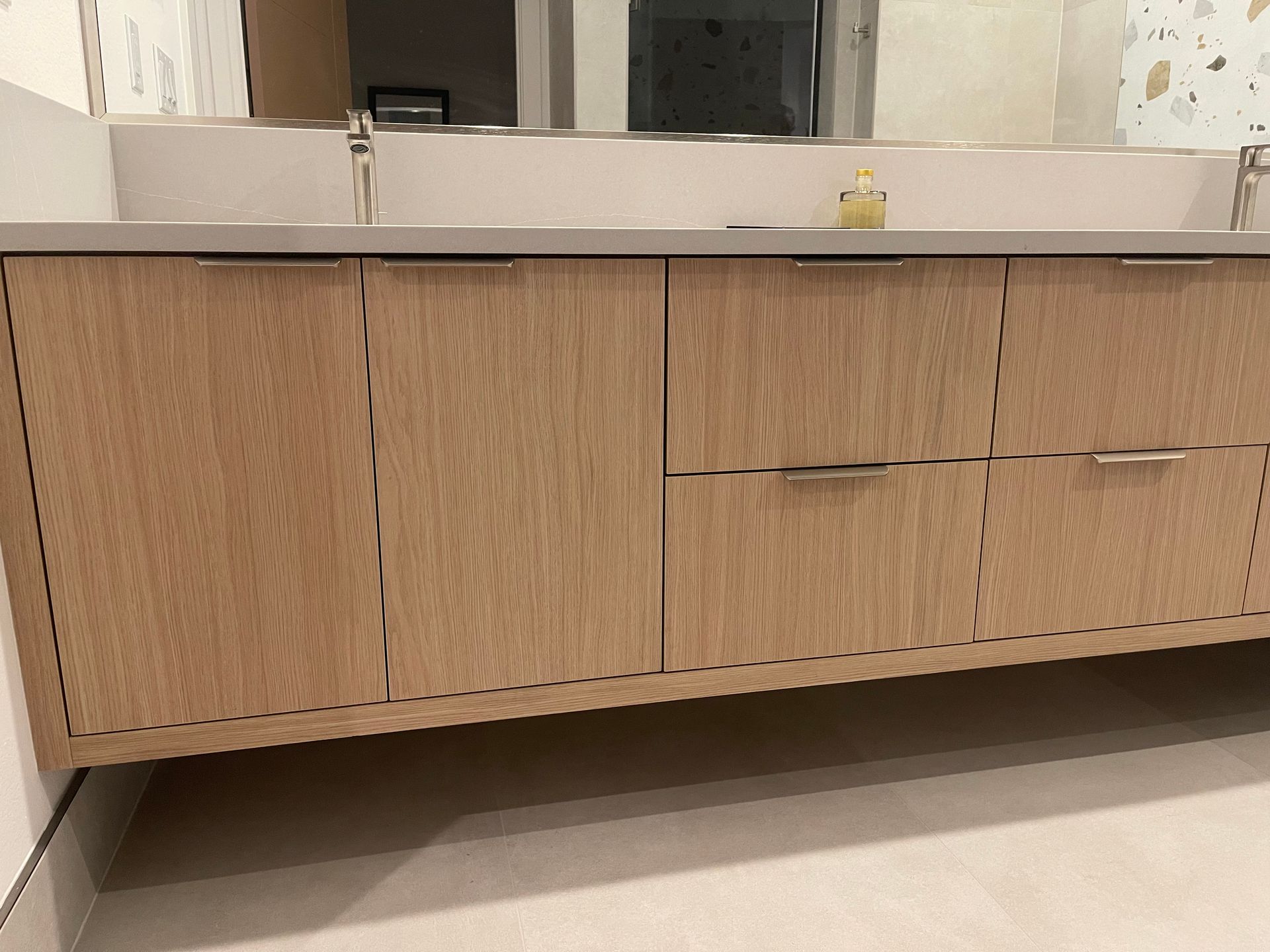 Wooden bathroom vanity with light stone countertop and silver hardware.