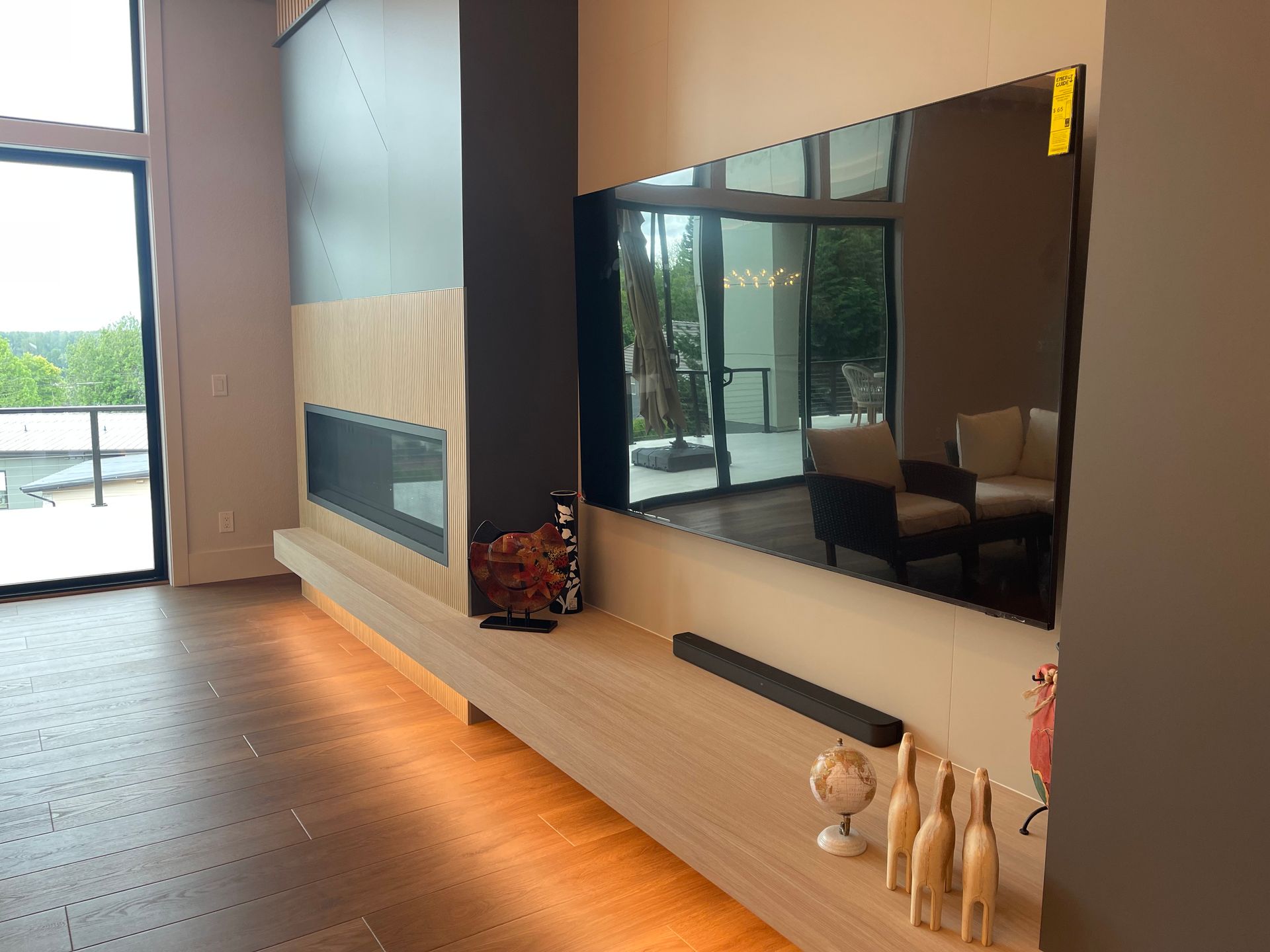 Living room with a large television mounted over a fireplace and wooden shelf with decor.