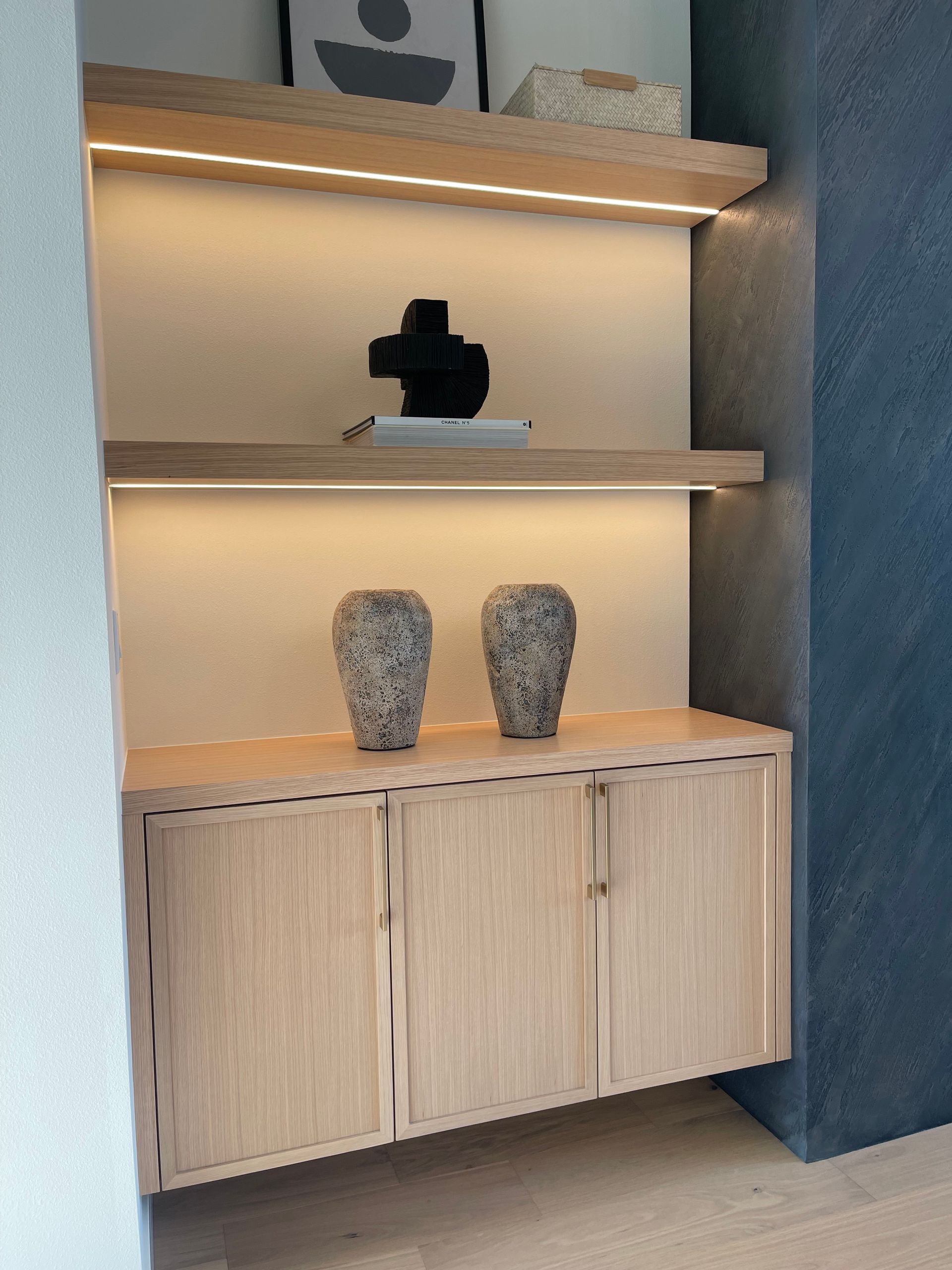 Modern built-in shelf display with warm lighting, wooden cabinets, and two decorative vases.
