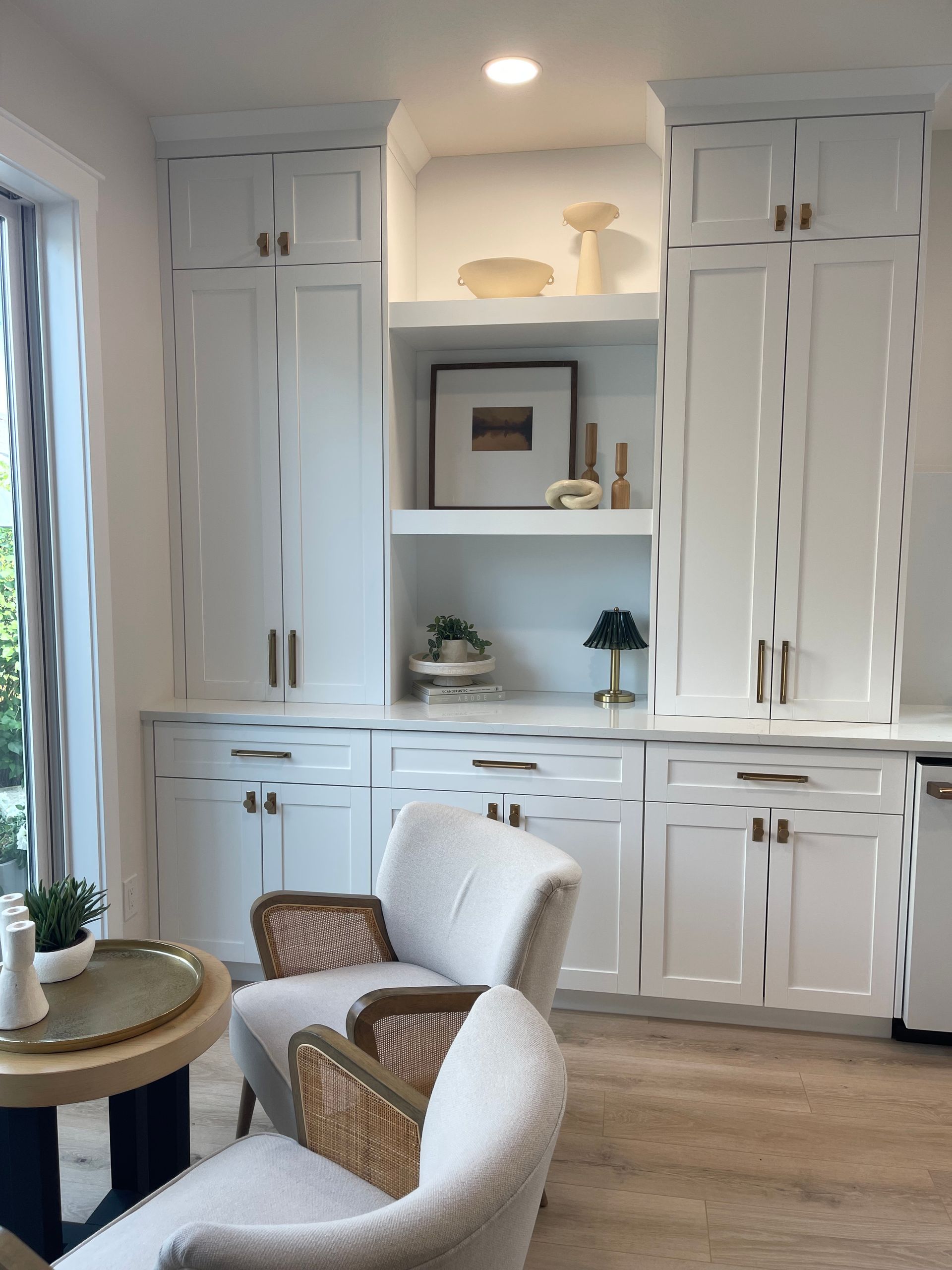 White built-in cabinets and shelves in a bright living room with two cream chairs and a small side table.