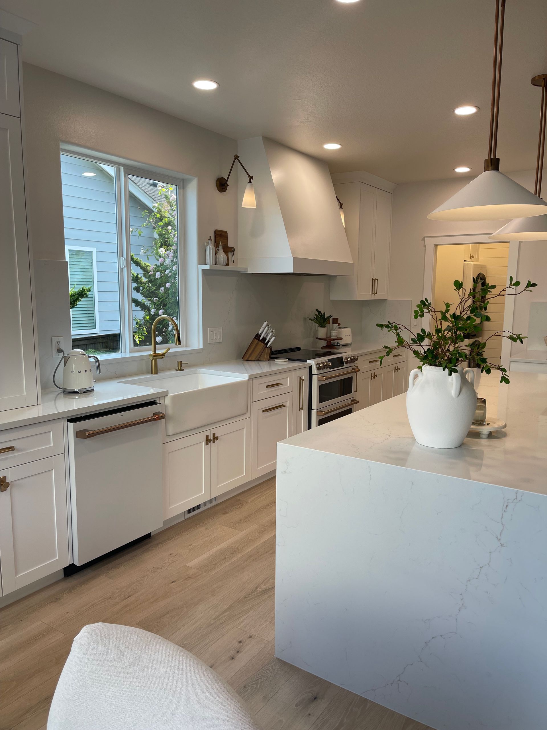 Bright white modern kitchen with island, large window, and stainless steel appliances