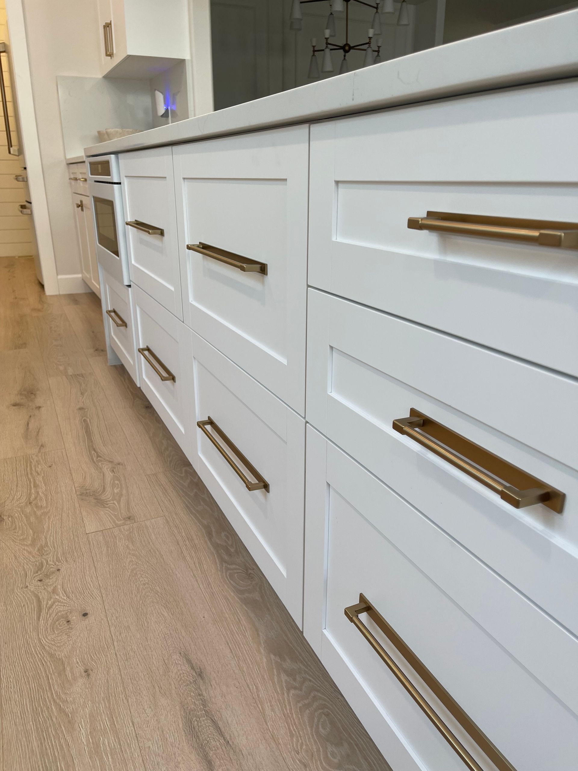 White kitchen cabinets with brass handles along a light wood floor, viewed from a low angle