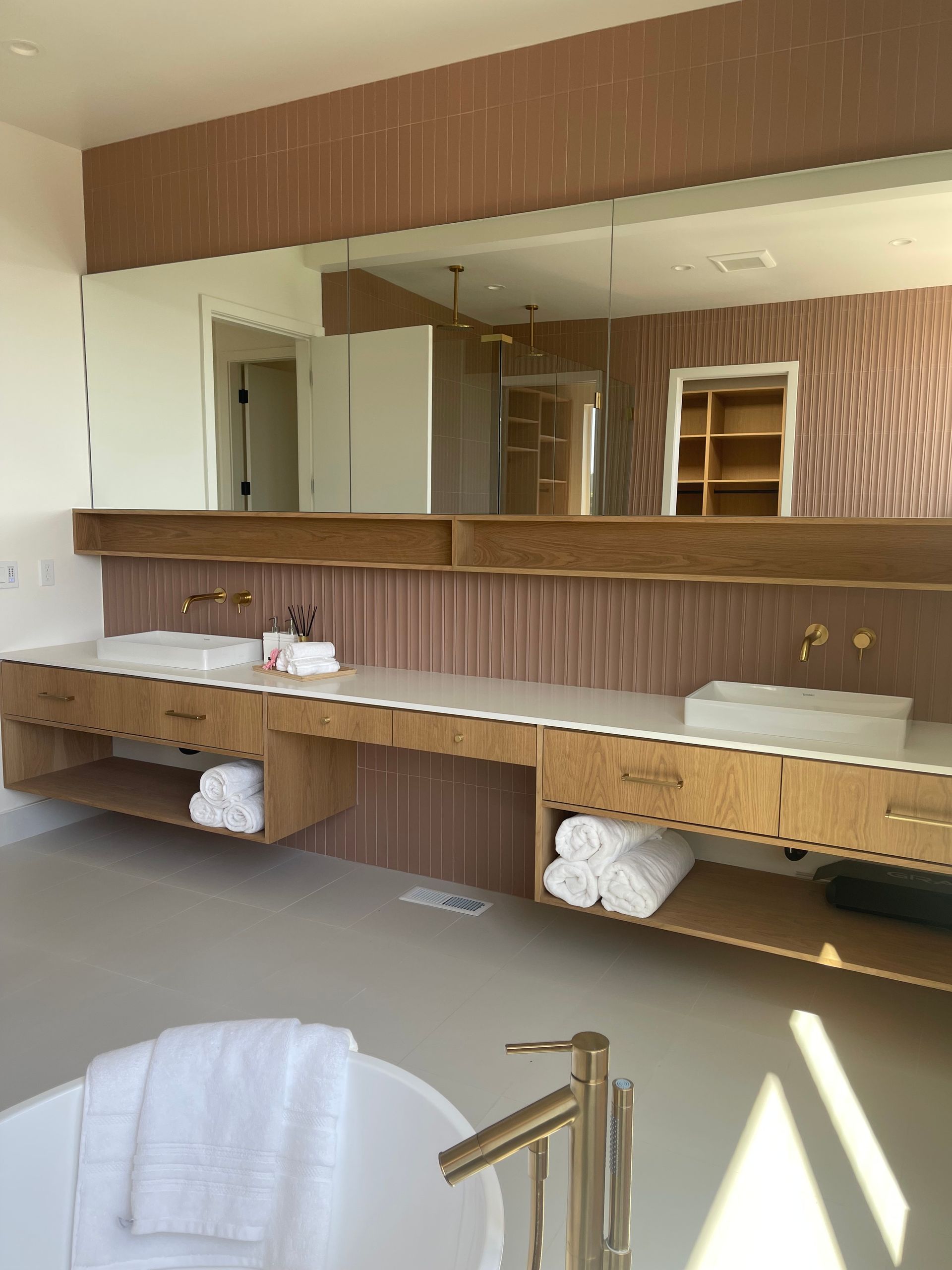 Modern bathroom with a double vanity, large mirror, and freestanding tub. Beige and gold accents.