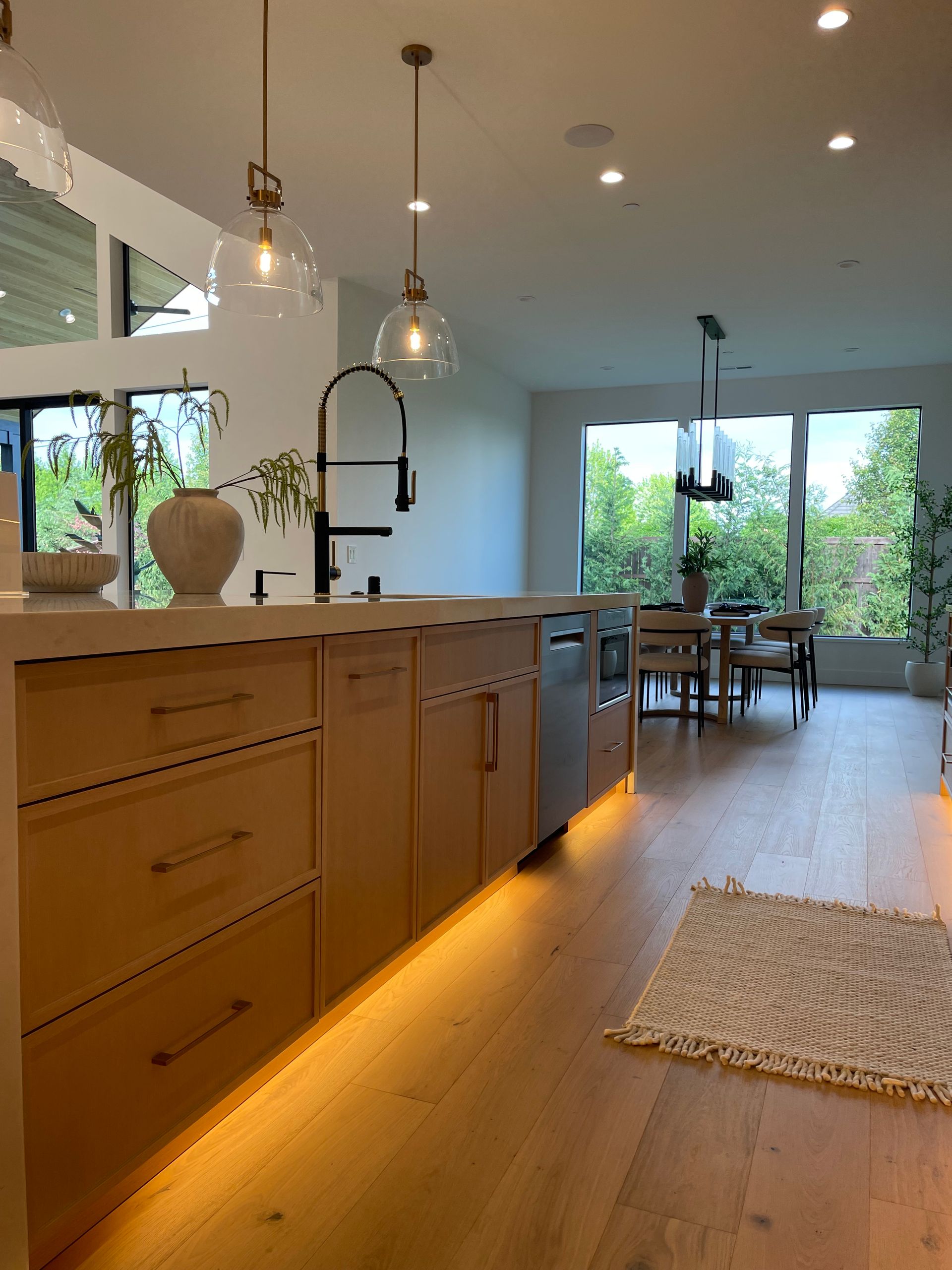 Modern kitchen with wood island, pendant lights, warm under-cabinet lighting, and dining area by large windows in Oregon, WA