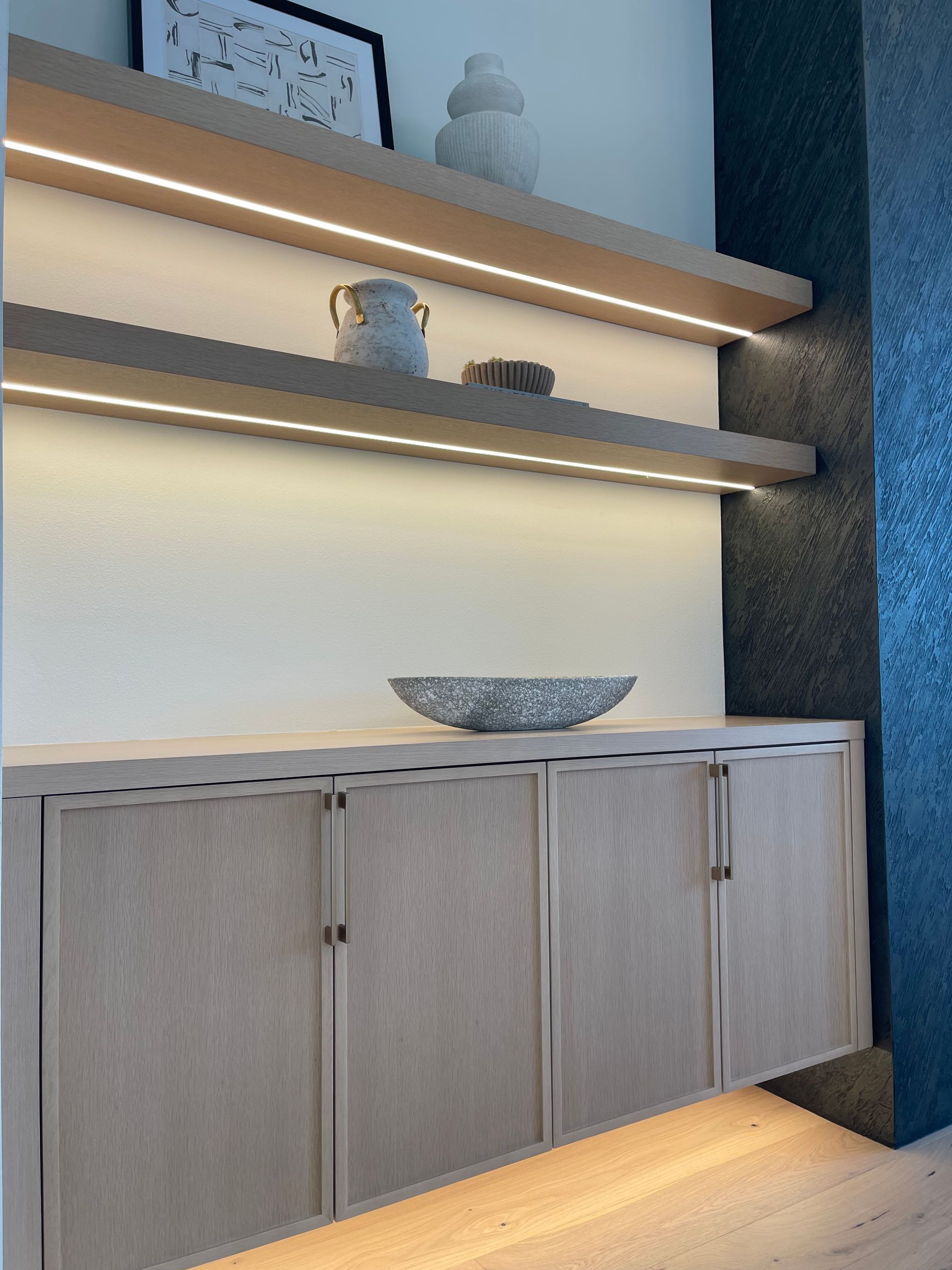 Modern kitchen sideboard with wood cabinets, lit floating shelves, and decorative bowls. in Portland, Oregon