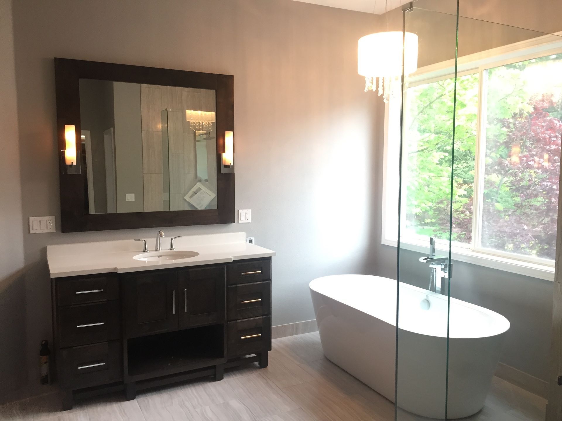 Bathroom with dark wood vanity, white tub, large mirror, and a window with greenery.