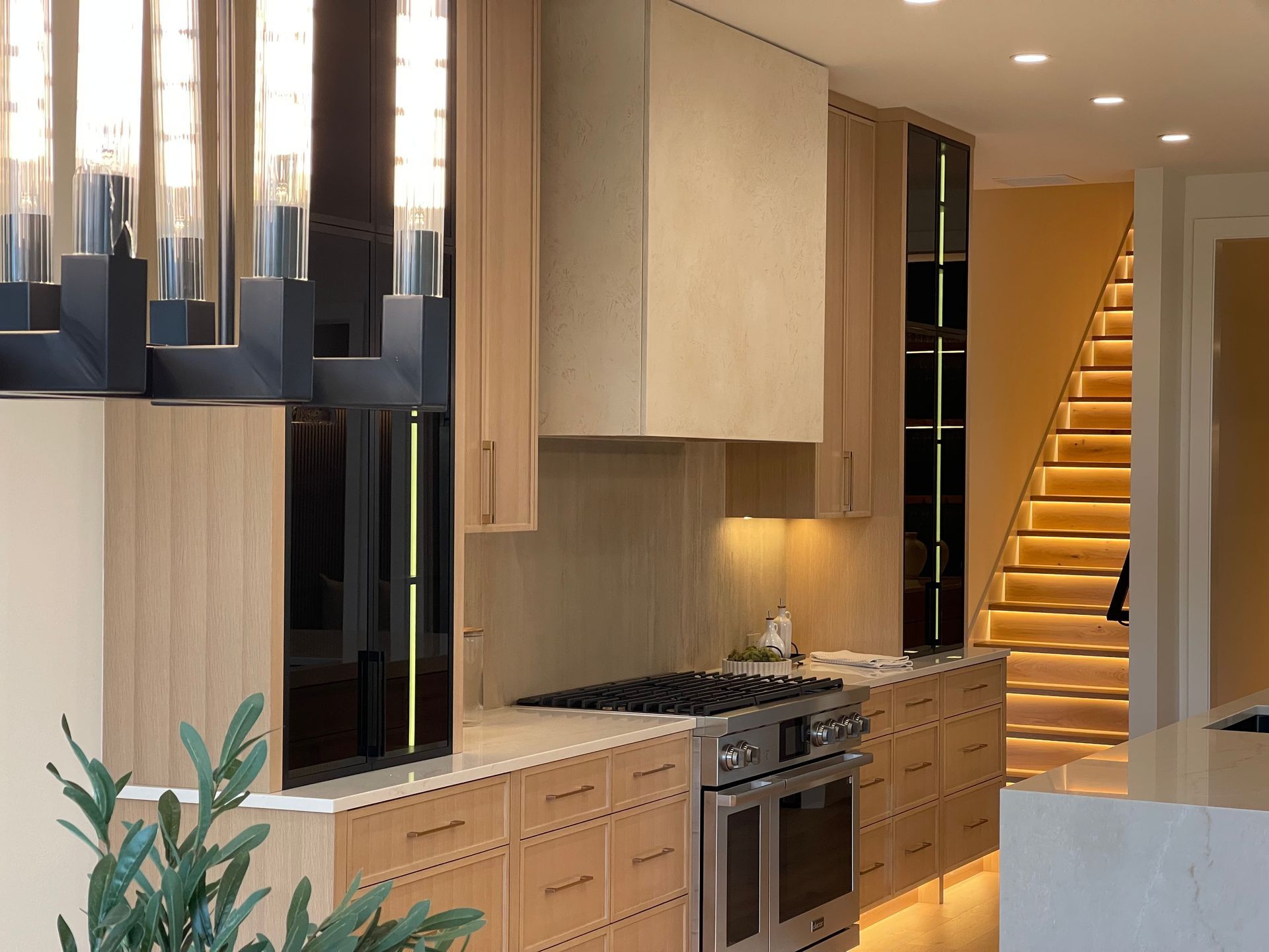 Modern kitchen with light wood cabinets, stainless steel stove, and illuminated staircase in the background in Portland