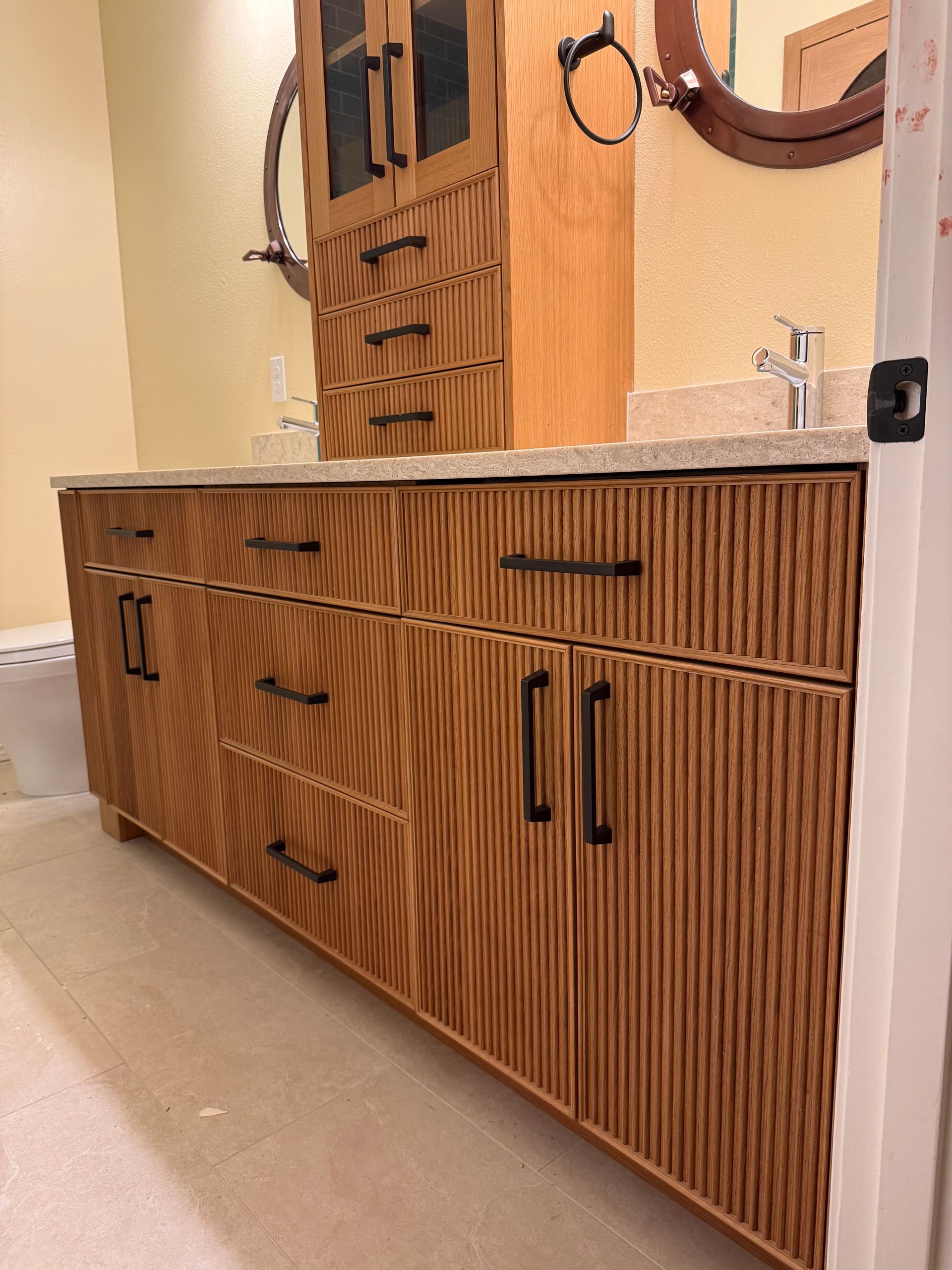 Bathroom with wooden vanity, cabinetry, mirror, and faucet fixtures. Light tan color scheme.