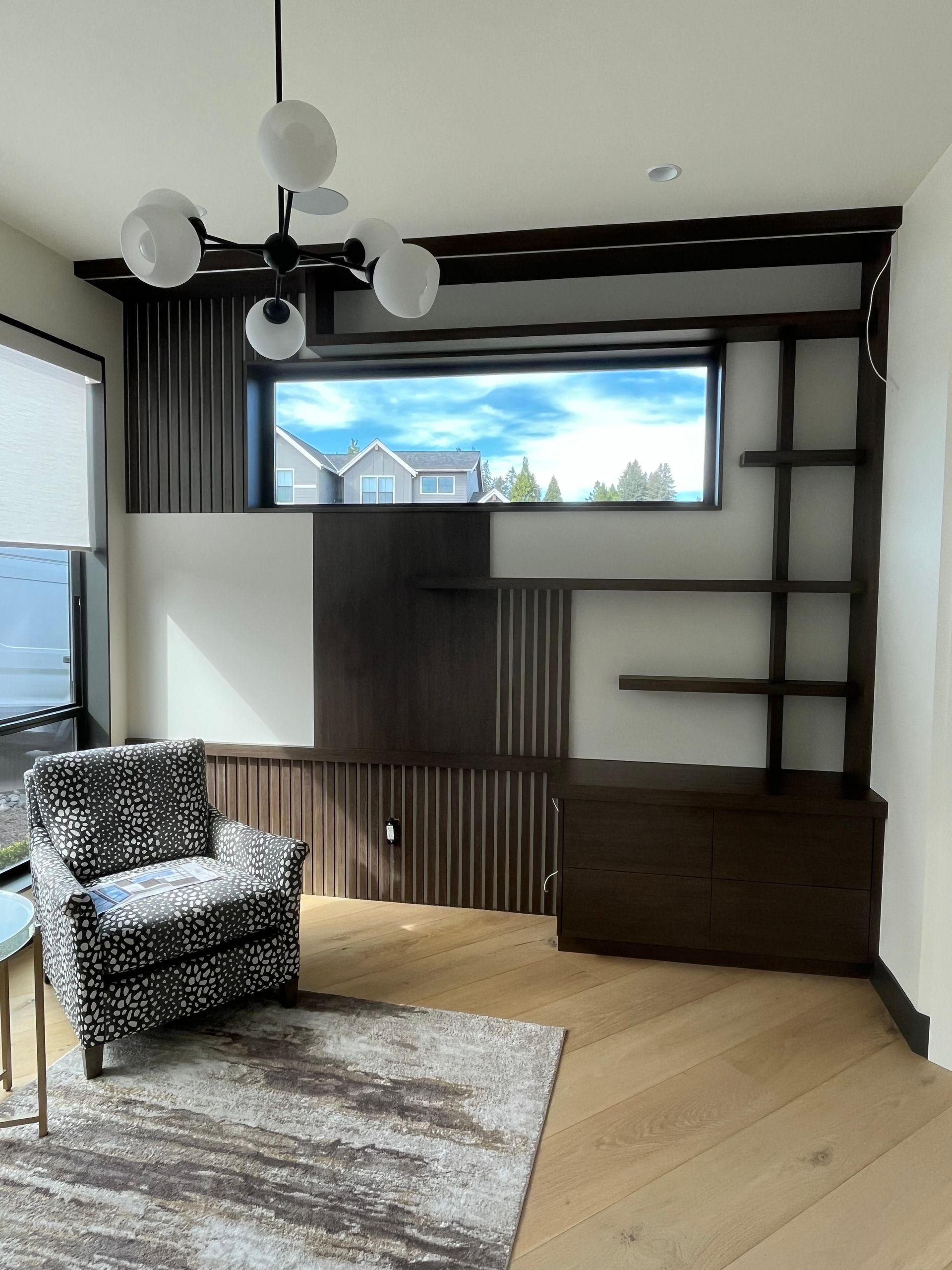 Modern room with dark wood built-in shelving, patterned chair, window with a view.