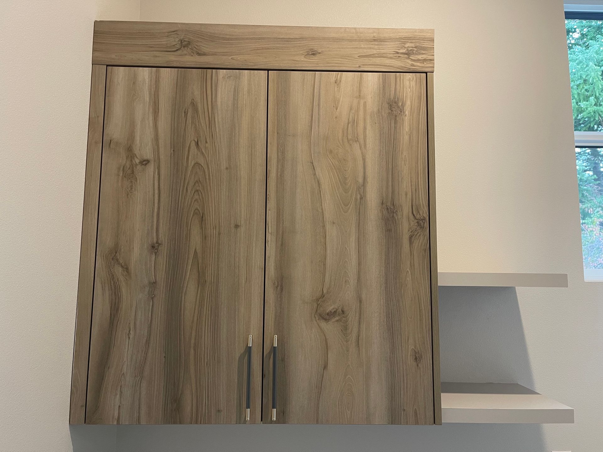 Laundry cabinet with two doors and two attached shelves on a white wall.