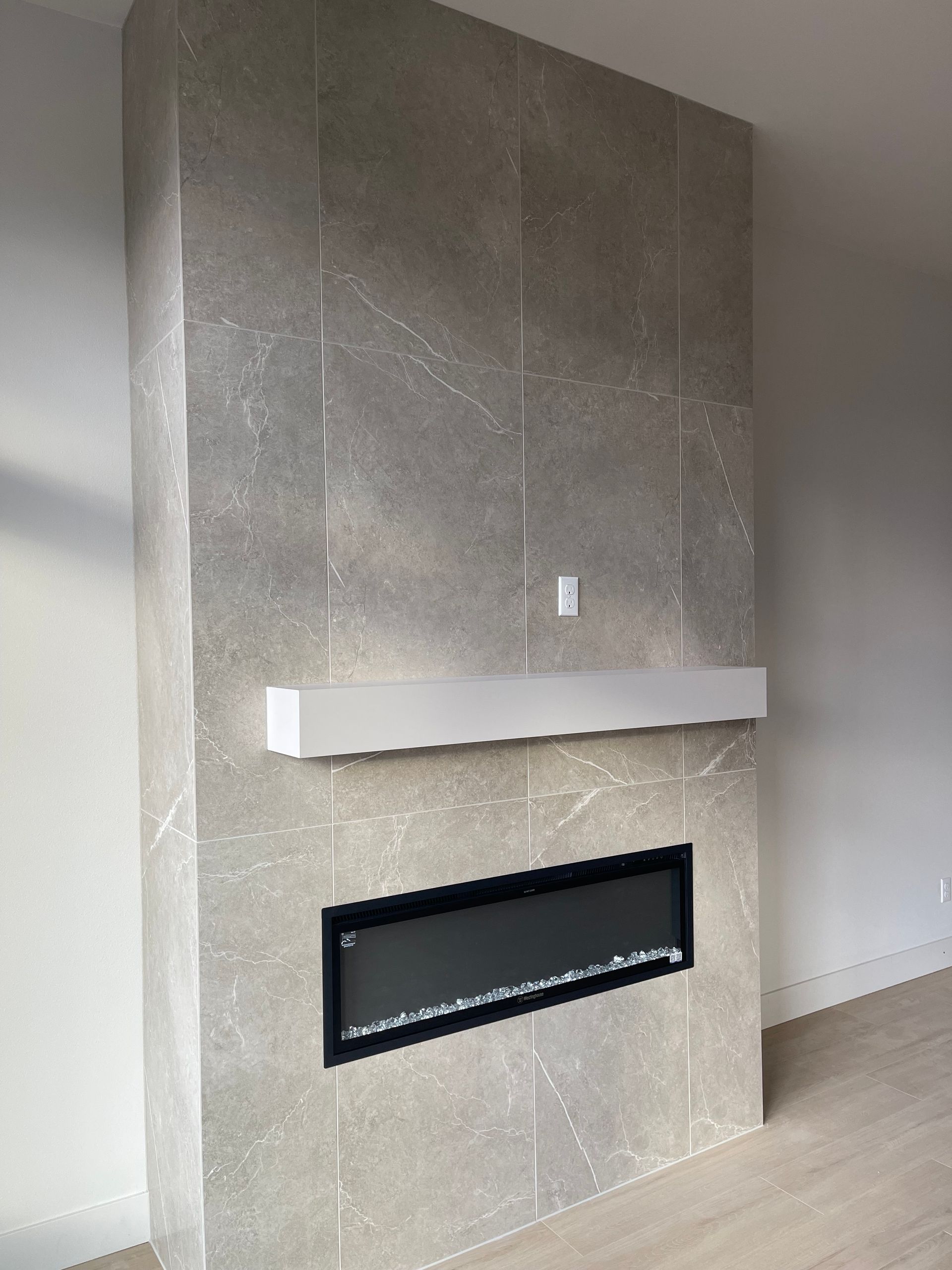 Gray tiled fireplace with black trim, white mantel, and electric fire display. custom floating shelves in Portland