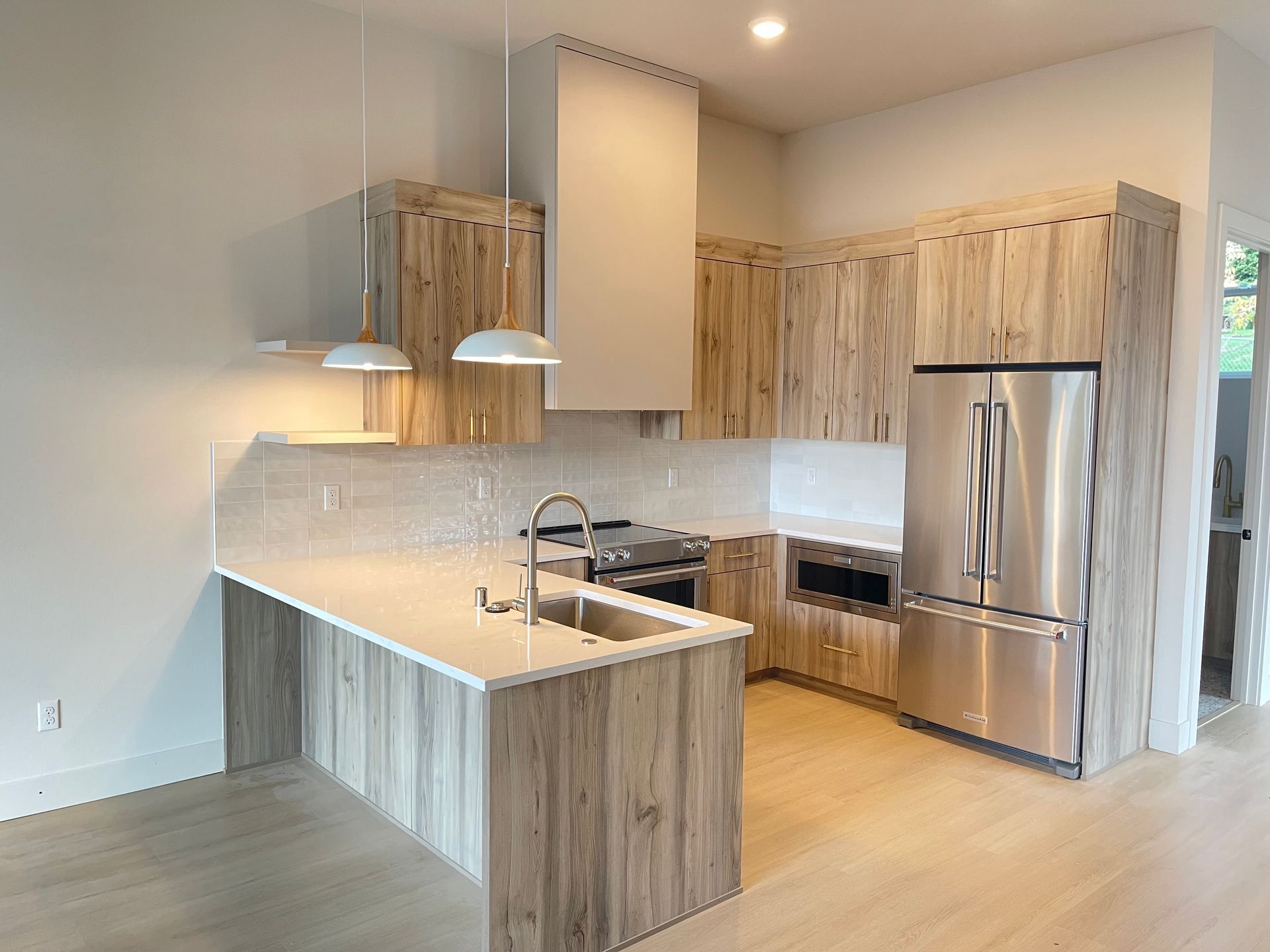 Modern kitchen with light wood cabinets, stainless steel appliances, and white countertops.