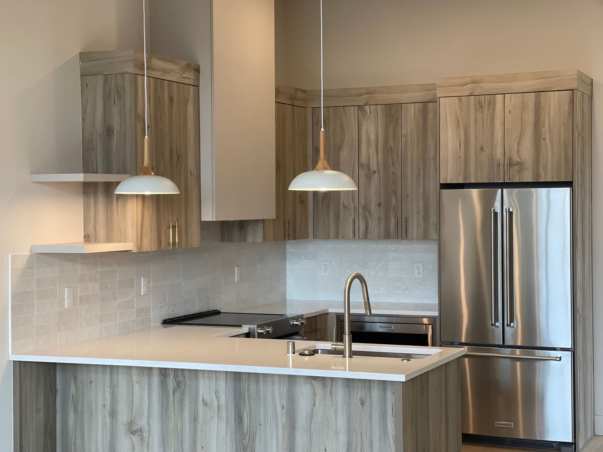 Modern oak kitchen with light wood cabinets, stainless steel appliances, and white pendant lights.