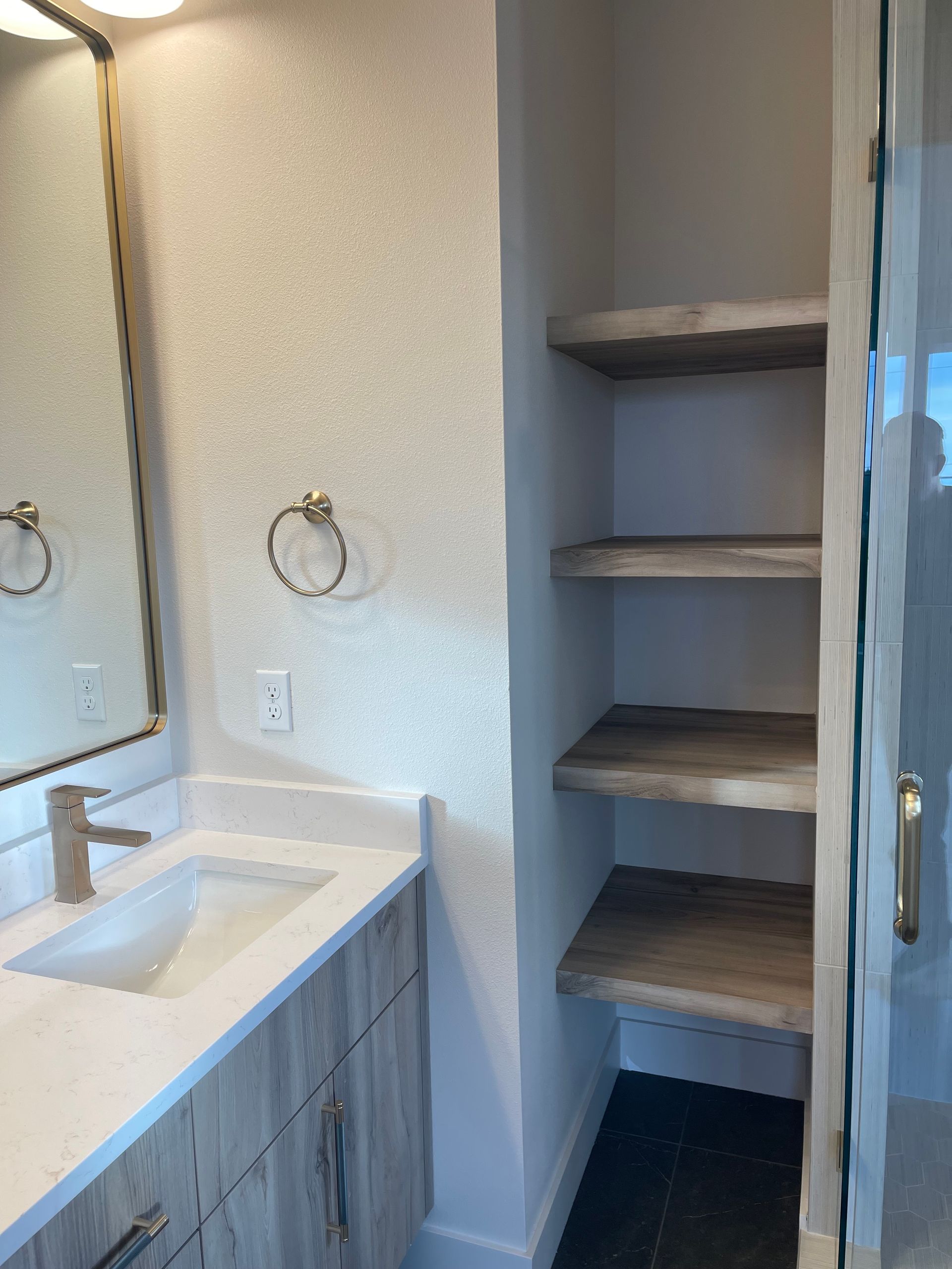 Bathroom with vanity, mirror, and shelves inside a shower with a glass door. custom kitchen manufacturing in Portland