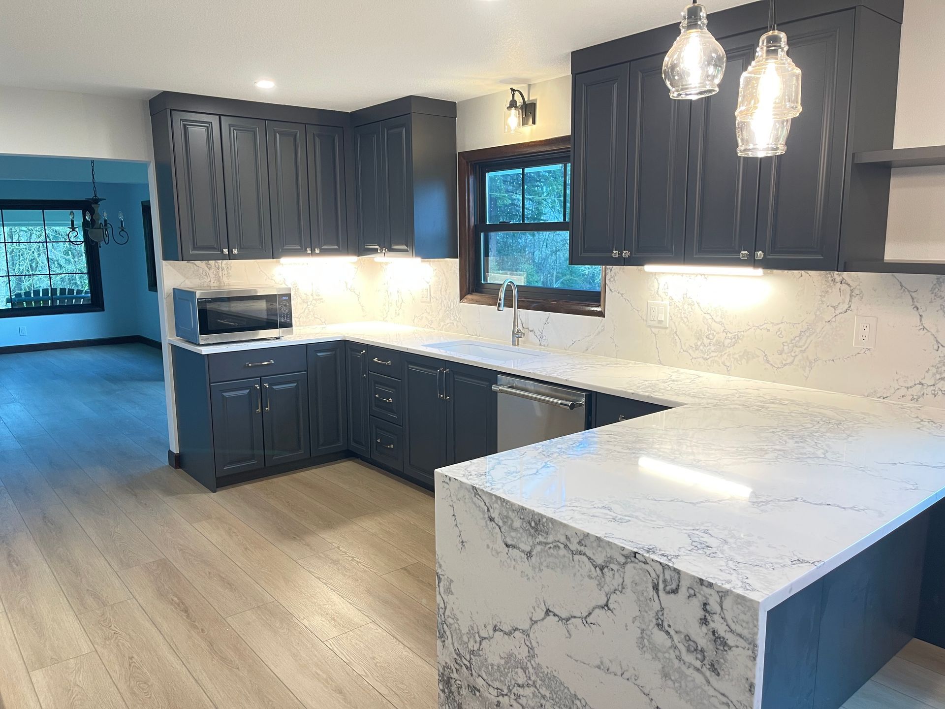Dark blue kitchen cabinets, white countertops, stainless steel appliances, and wood floors. made Pro-techwoodworking.