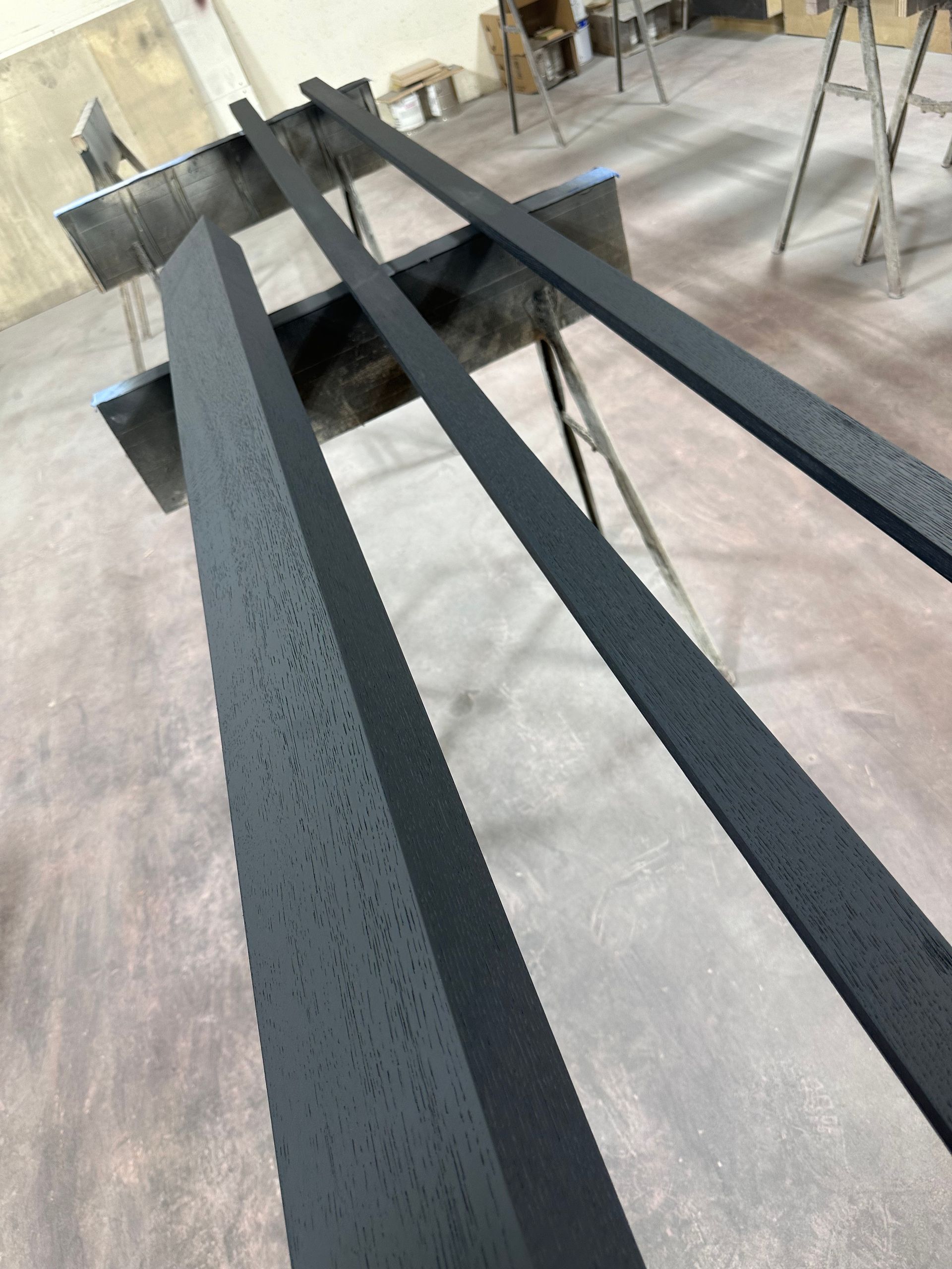 Black painted wooden boards on sawhorses in a workshop, showing slight texture imperfections.