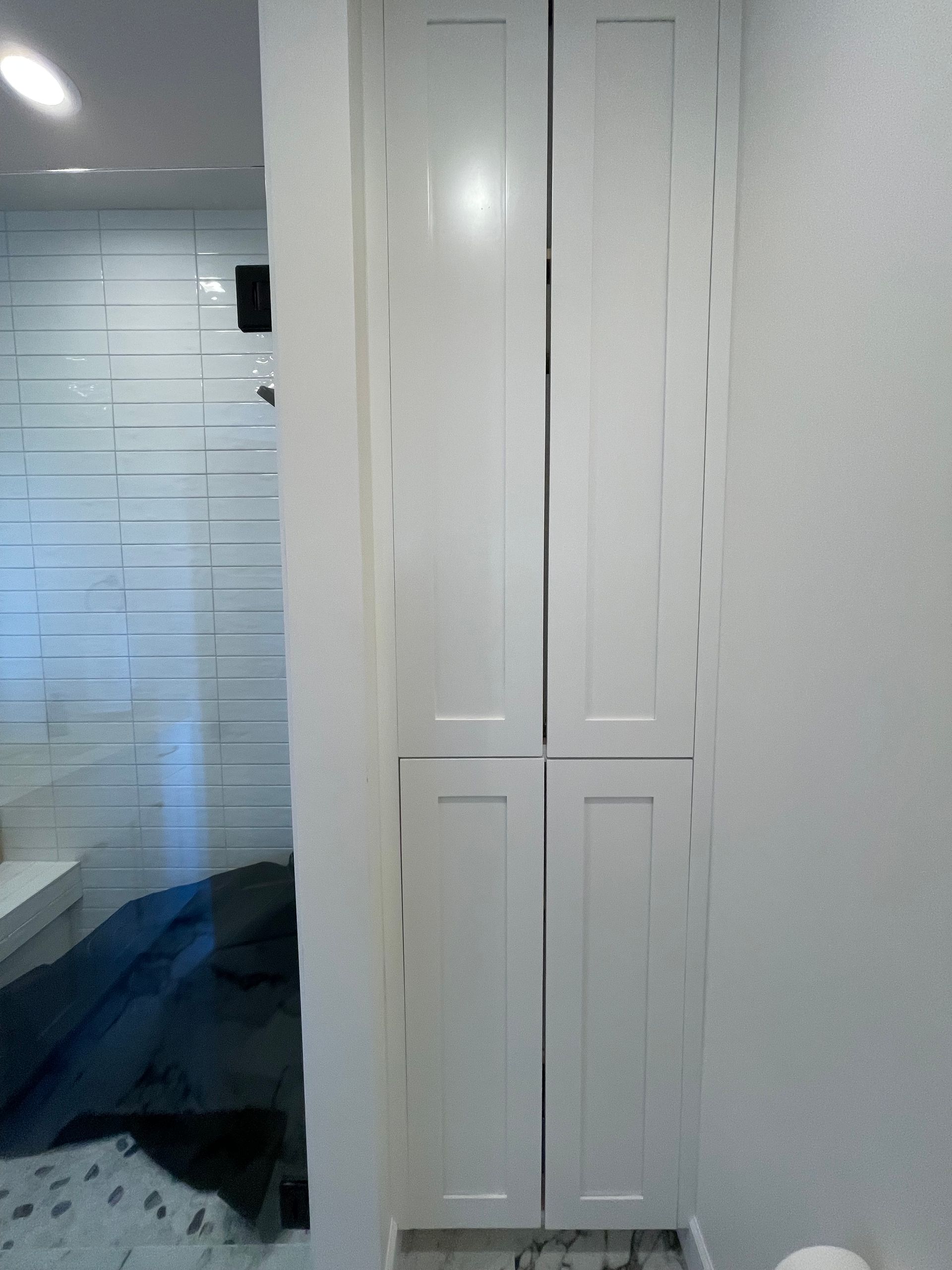 White, paneled closet doors in a narrow space between a wall and a tiled wall.