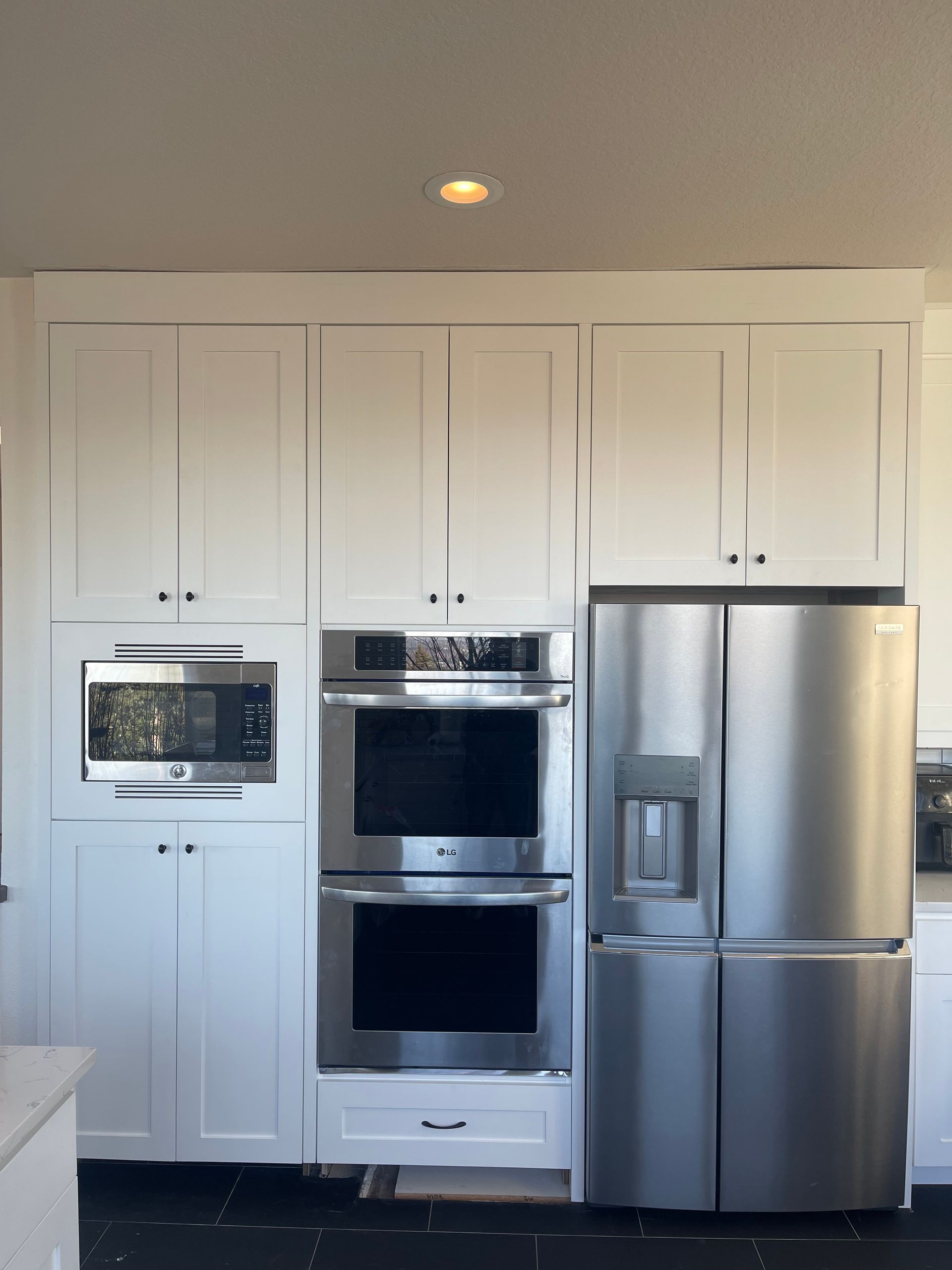 White kitchen cabinets with built-in stainless steel appliances: microwave, double oven, and refrigerator.