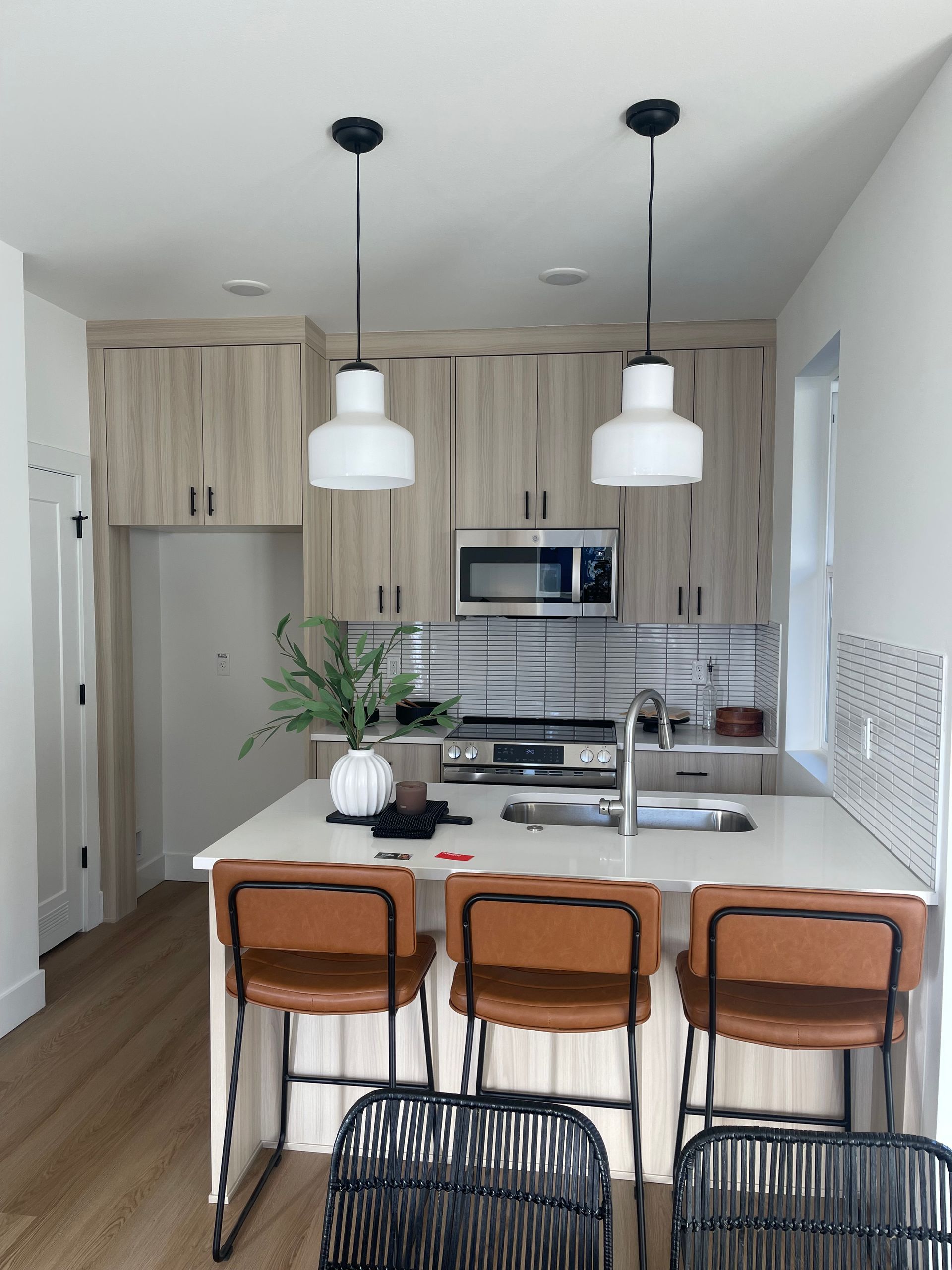 Kitchen with island, light wood cabinets, white countertops, black pendant lights, and brown bar stools pro-techwoodwoorking.