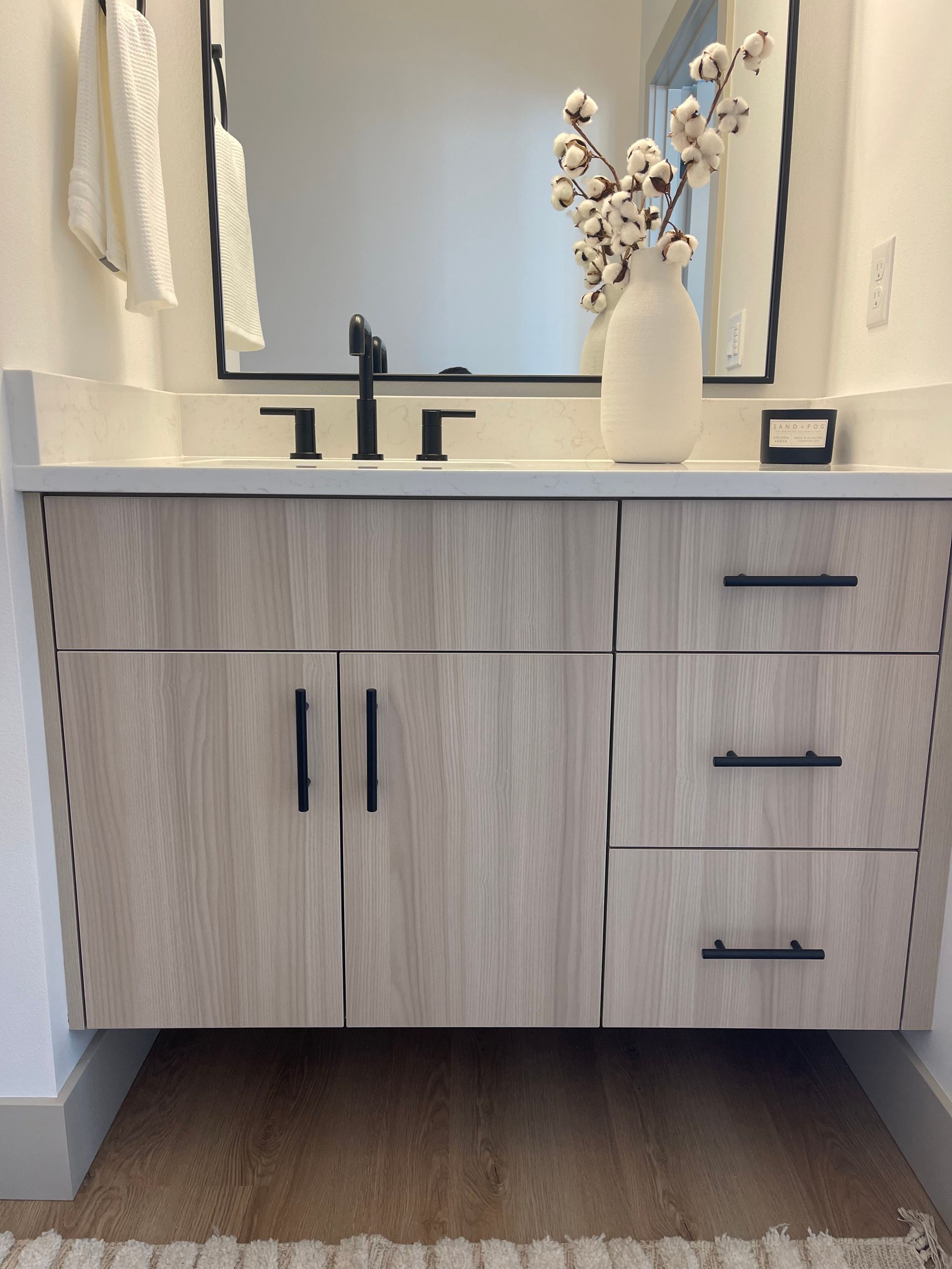 Light wood bathroom vanity with black hardware, mirror, and vase of cotton pro-techwoodwoorking