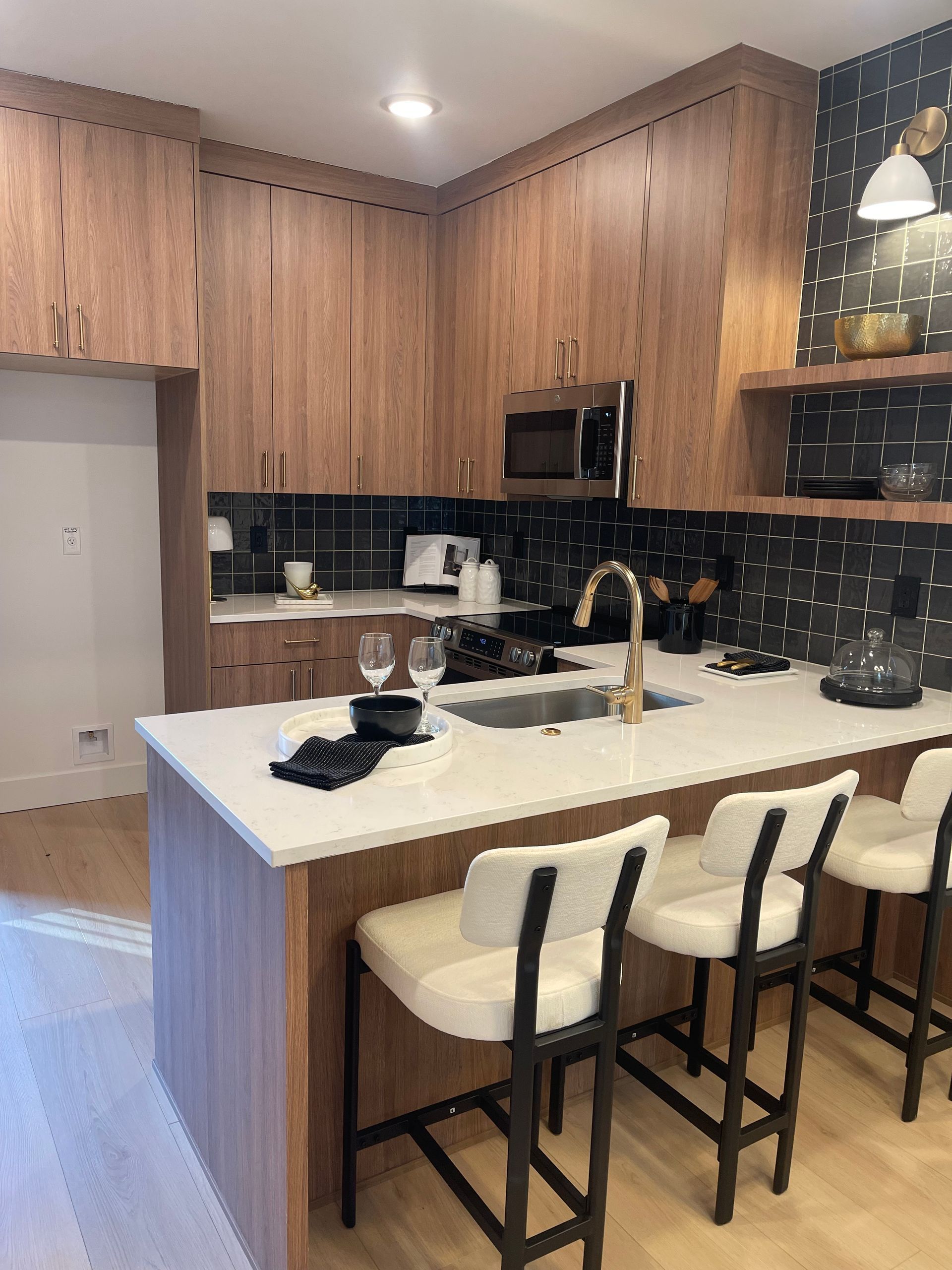 Modern kitchen with wood cabinets, white island with bar stools, gold faucet, and black backsplash pro-techwoodwoorking.