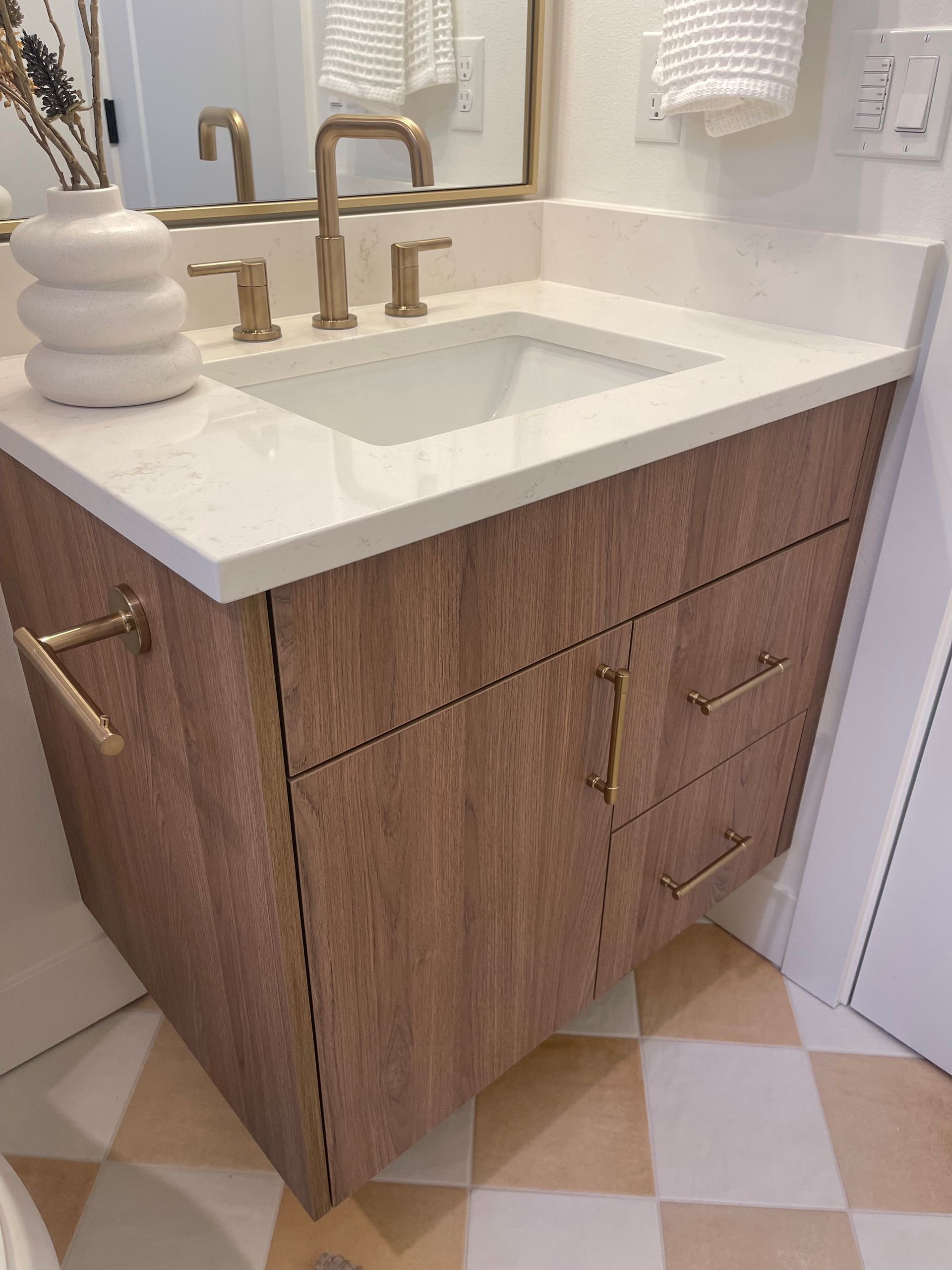 Bathroom vanity with wood grain cabinet, white countertop, gold fixtures, and patterned floor pro-techwoodwoorking.