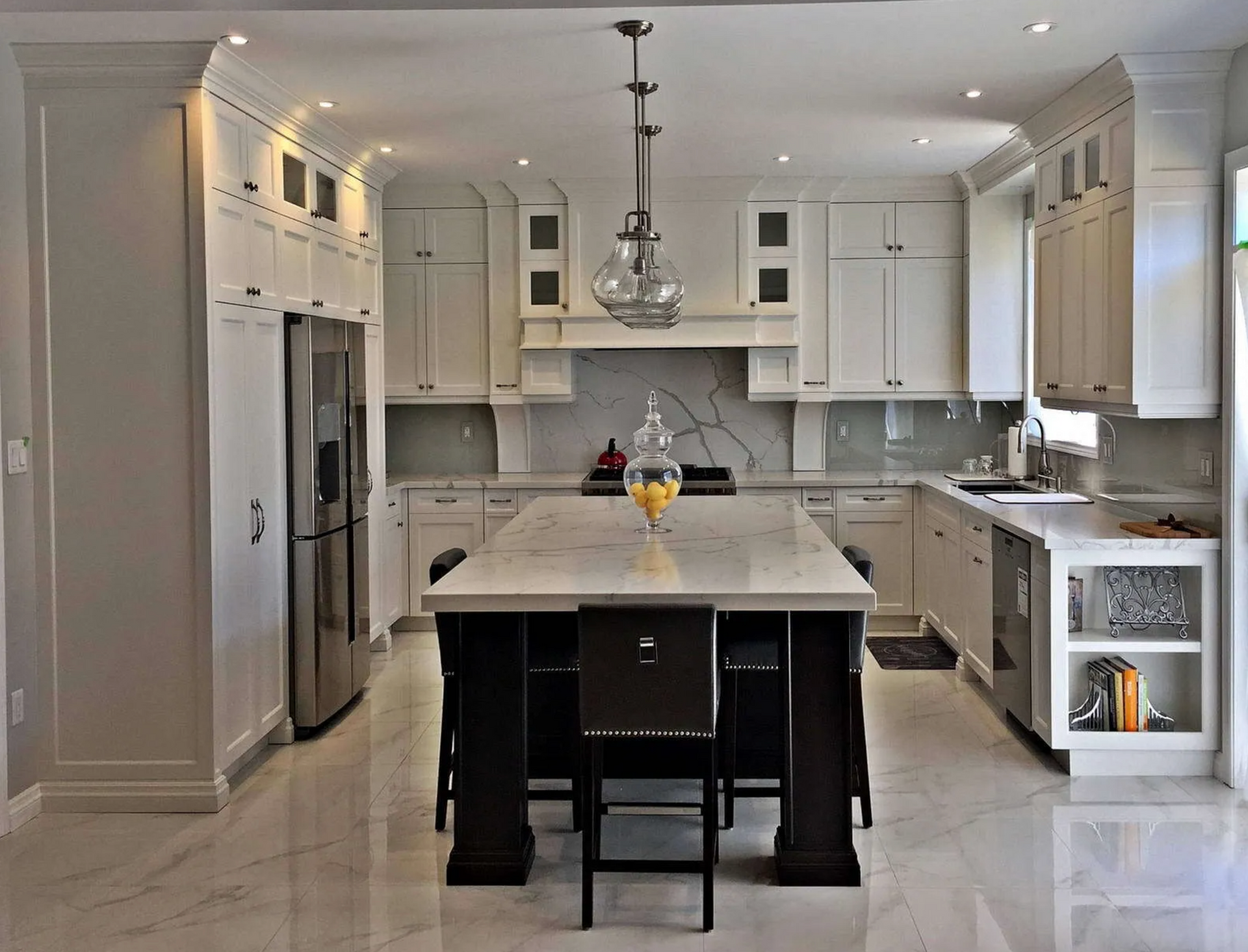 Elegant white kitchen with marble island, stainless steel appliances, and dark chairs.