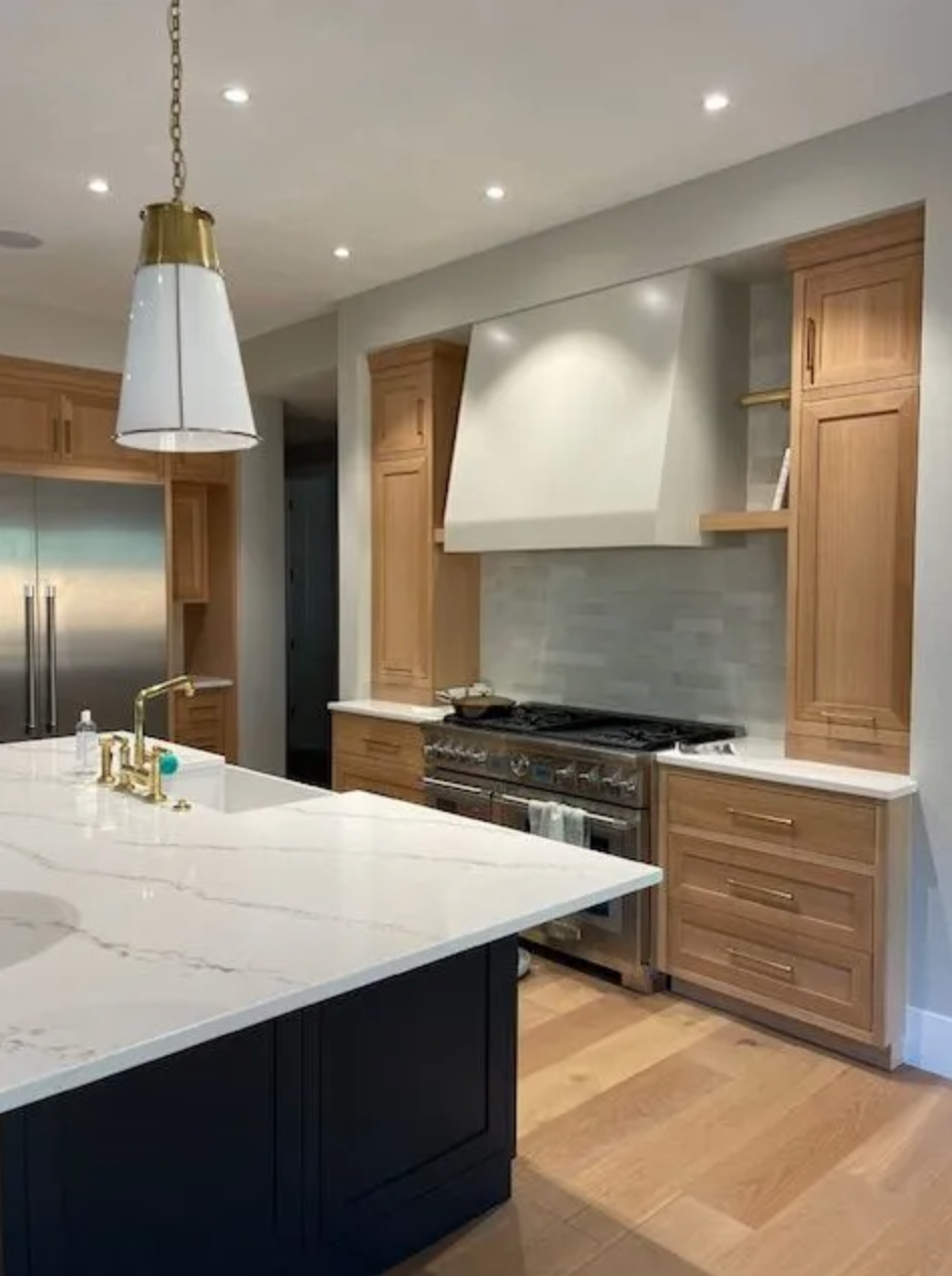 Warm wood cabinets in Portland with white hood, tile backsplash, and built-in lighting