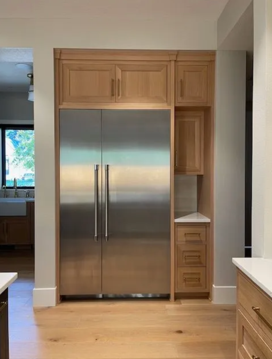 Stainless steel refrigerator built into light wood cabinetry in a kitchen.
