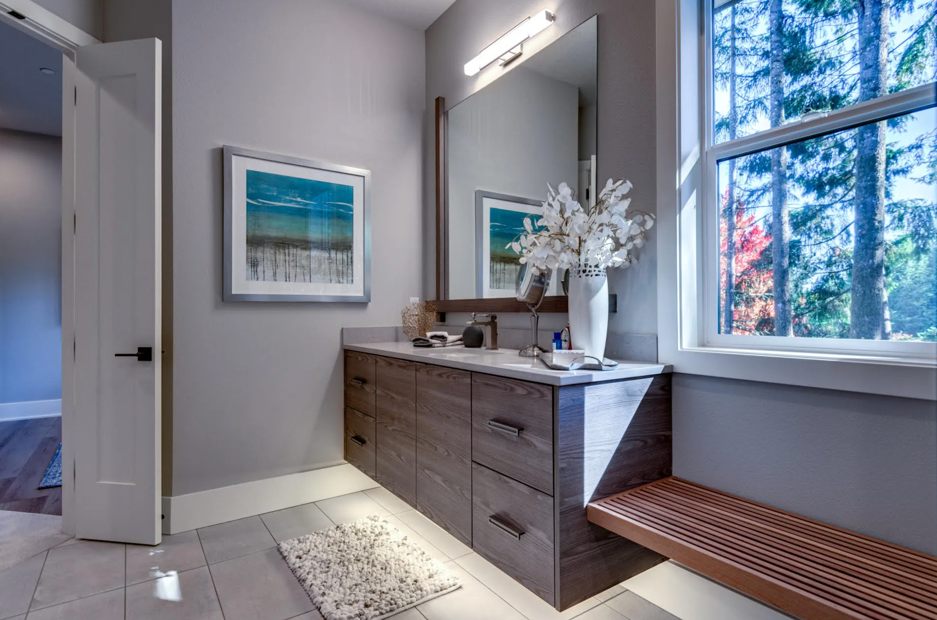 Modern bathroom with floating vanity, large mirror, and window overlooking trees.