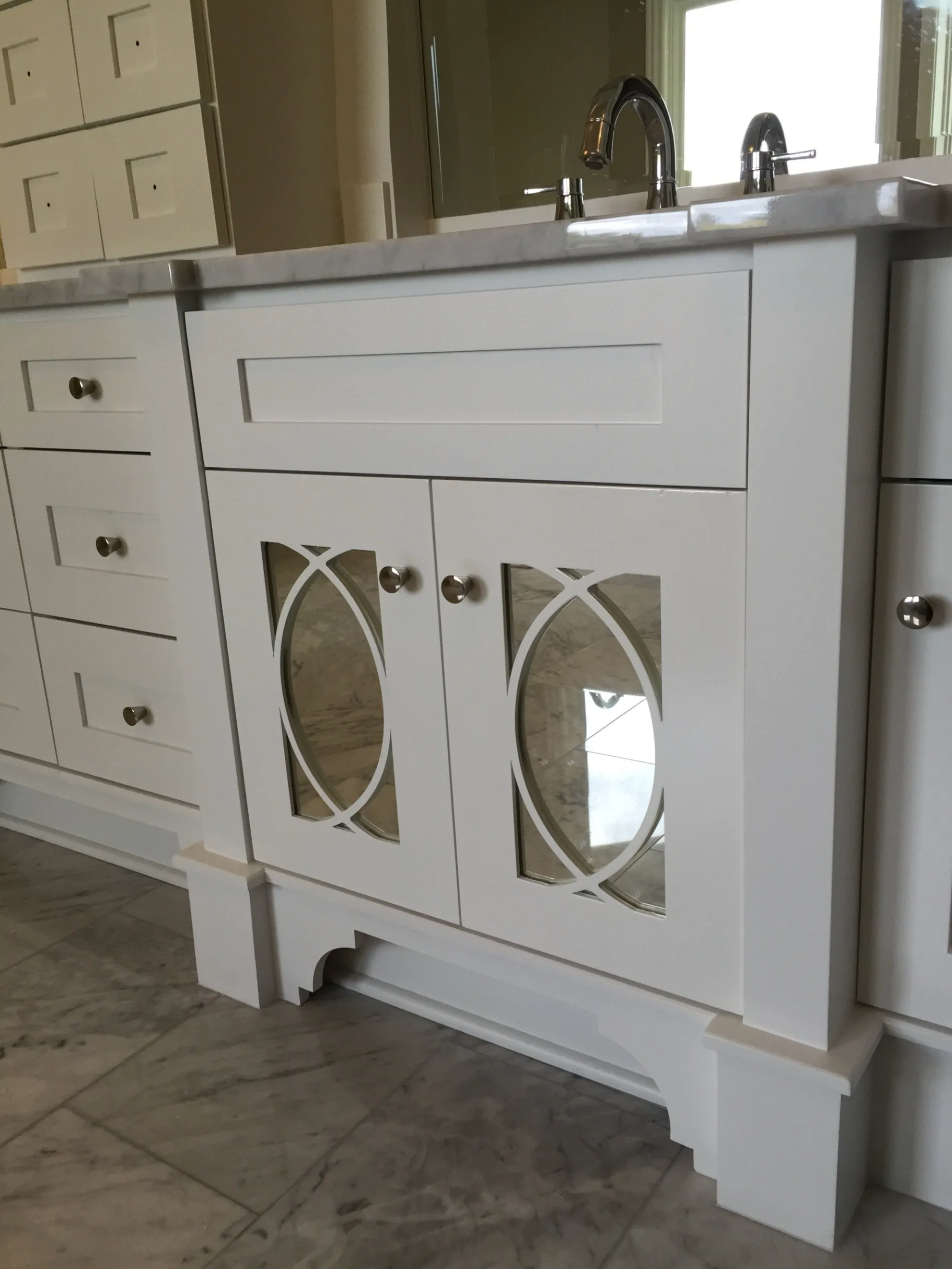 White bathroom vanity with oval mirrored cabinet doors, silver hardware, and marble countertop.