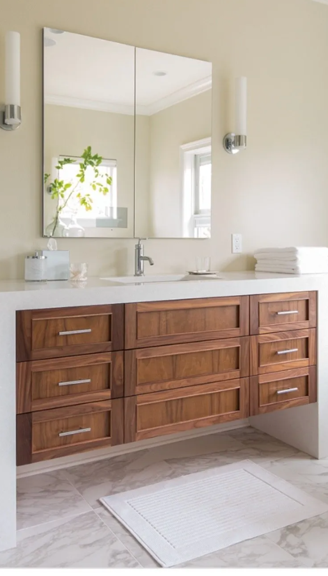 Bathroom vanity with wood drawers, white countertop, large mirror, and sconces.