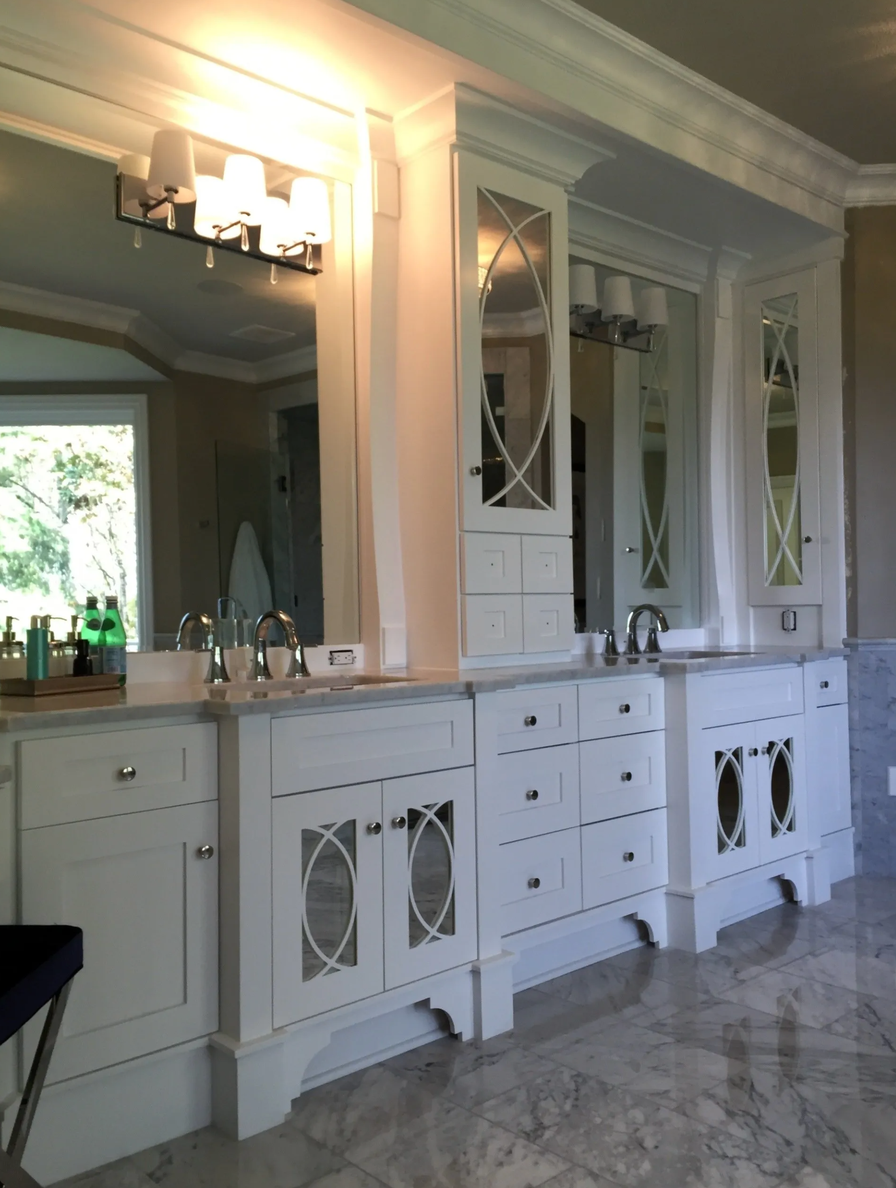 White bathroom vanity with marble countertop and decorative cabinets; large mirror and lighting.