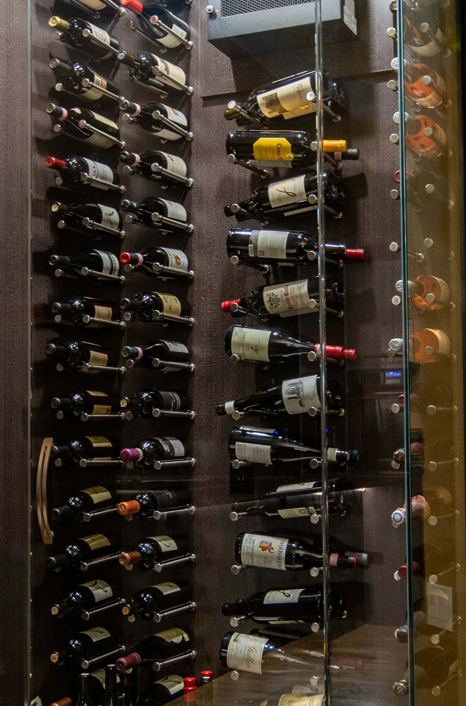 Wine bottles stored in a climate-controlled wine cellar, with rows of dark bottles on wooden racks.