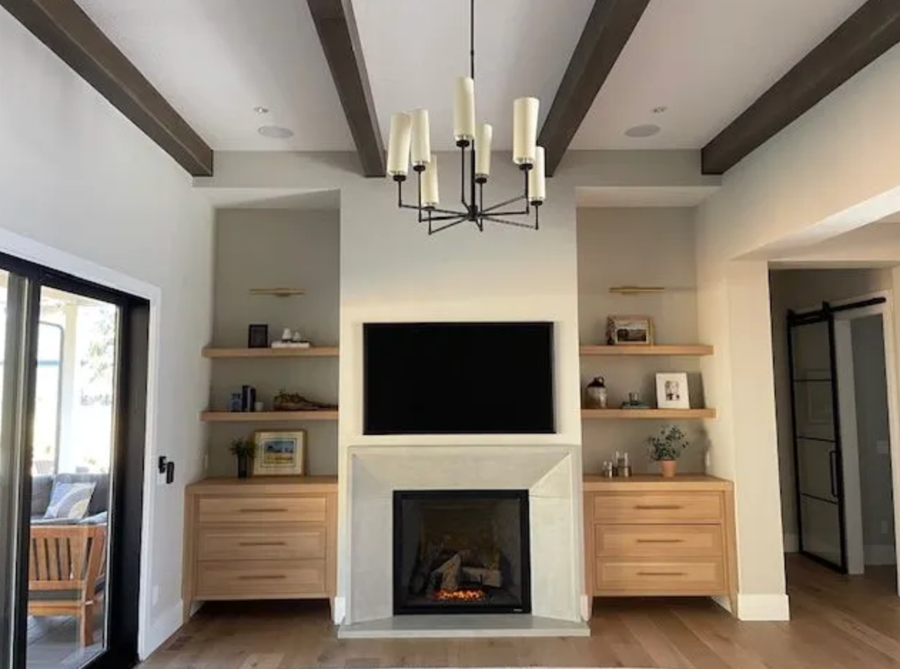 Living room with fireplace, TV, built-in shelves, light fixture, and wooden beams.