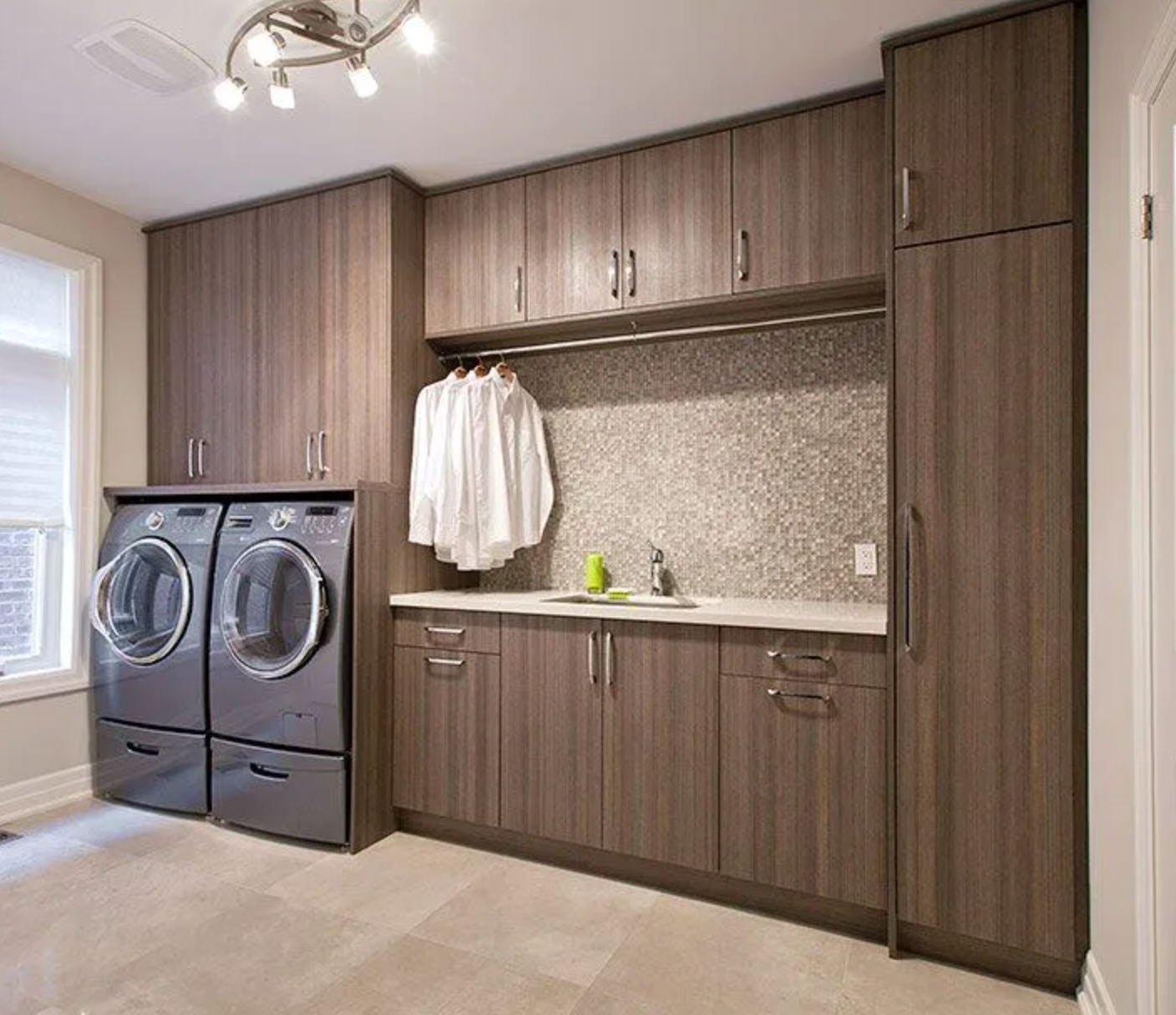 Dark wood laundry cabinets with granite backsplash and stacked washer-dryer
