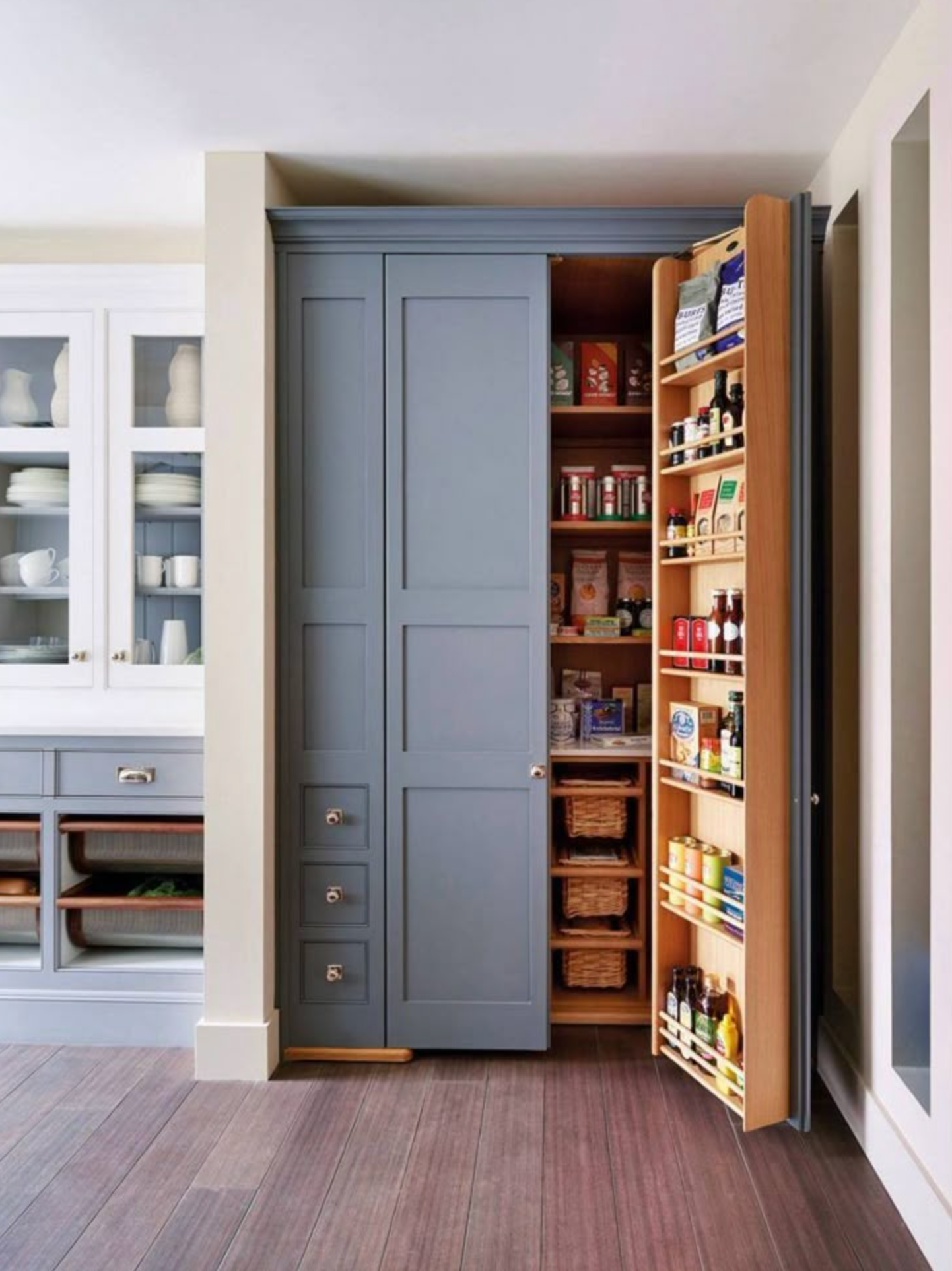 Blue kitchen pantry with pull-out shelves. Open cabinet with spices, food items, and drawers.